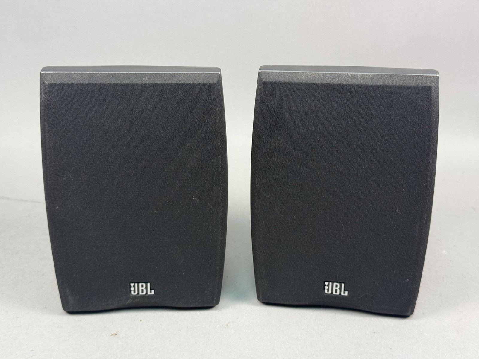 A Pair of JBL N24II Speakers: A pair of JBL Northridge Series N24II two-way bookshelf speakers featuring dark gray composite cabinets. Each unit is equipped with a front-firing bass reflex port, a textured cone woofer, and a
