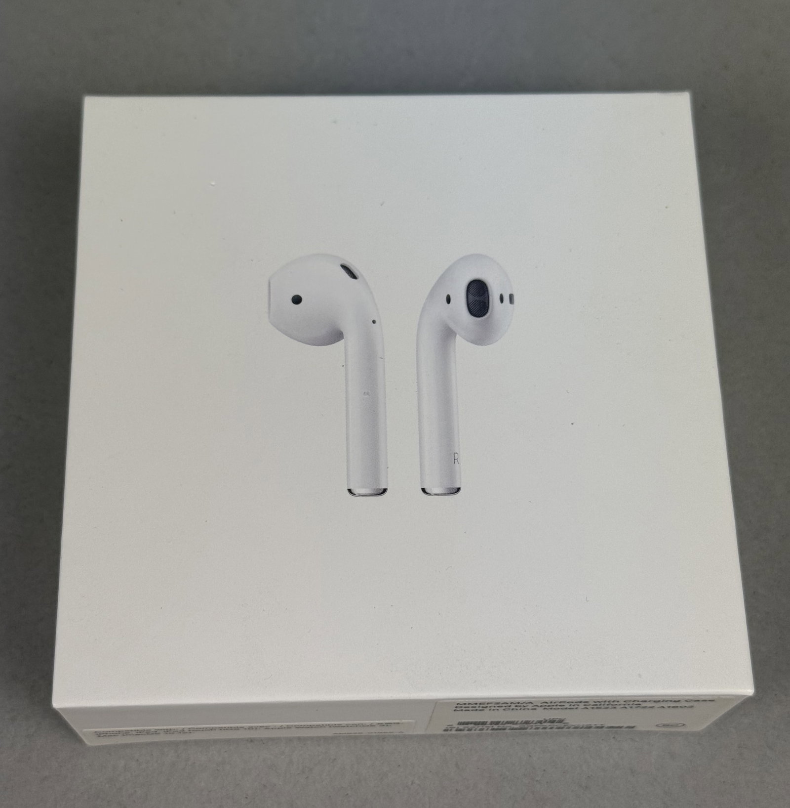 Apple AirPods With Case: A set of Apple AirPods comprising the left and right earbuds, a Lightning charging case, and the original retail packaging. The items are identified by model numbers A1523, A1722, and A1602, with the