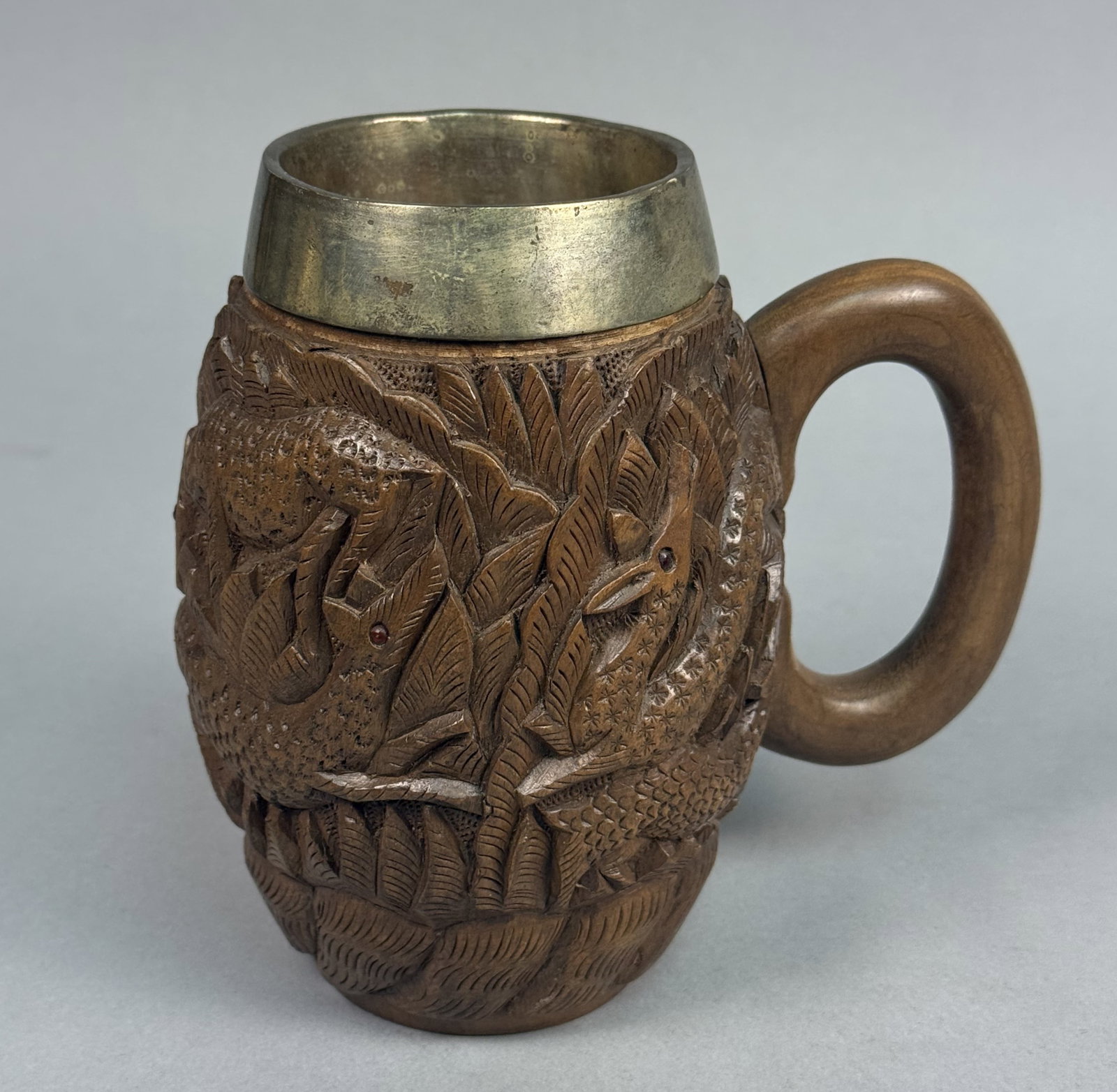 Carved Wood Deer Motif Tankard: This hand-carved wooden tankard features a high-relief wildlife scene of deer amongst dense foliage, accented by small inset glass bead eyes. The vessel includes a removable metal interior liner and