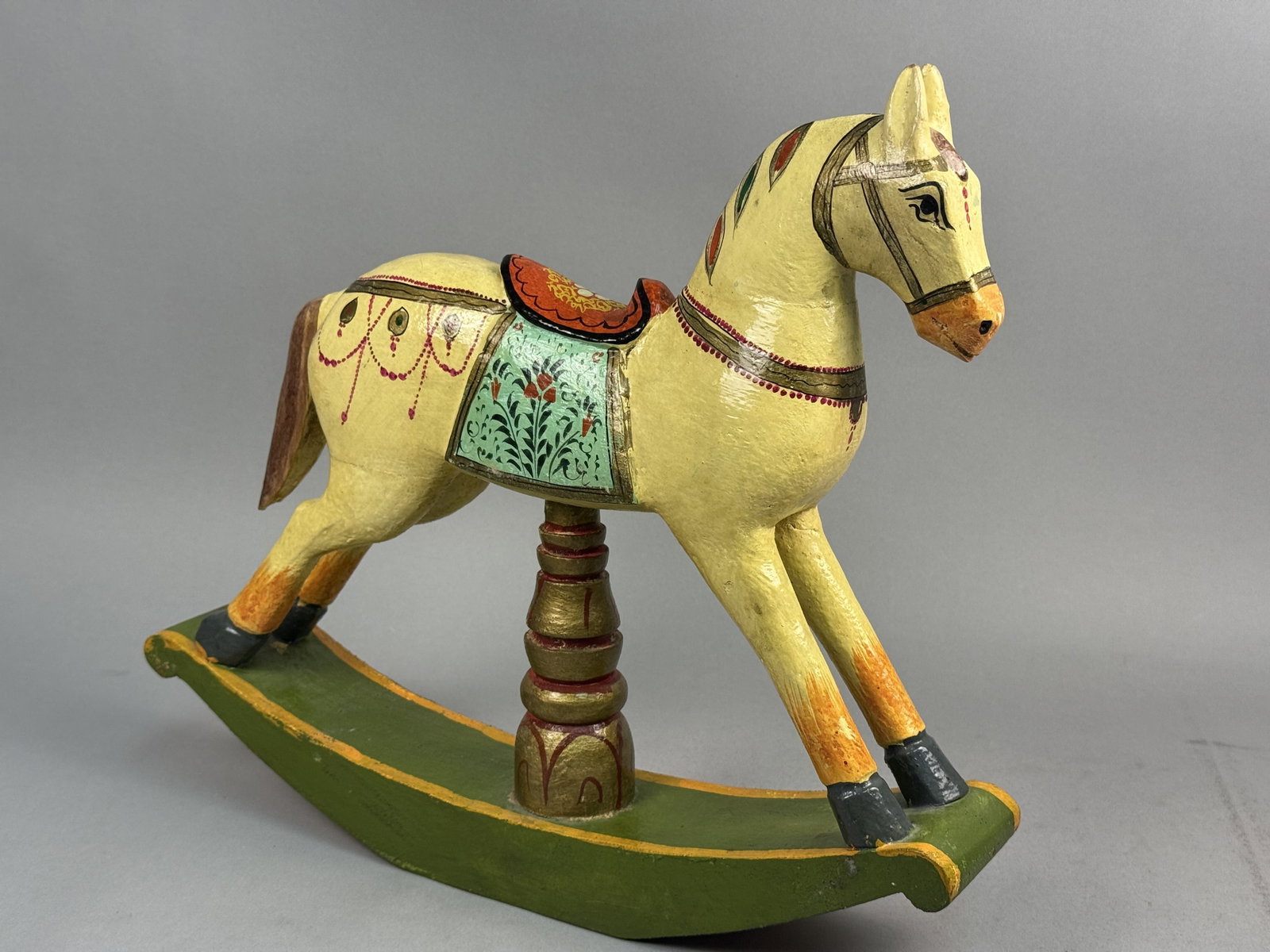 Hand-Painted Folk Art Rocking Horse: This hand-painted wooden rocking horse features traditional polychrome floral and geometric motifs in the Indian folk art style. The cream-colored figure displays a green floral saddlecloth and