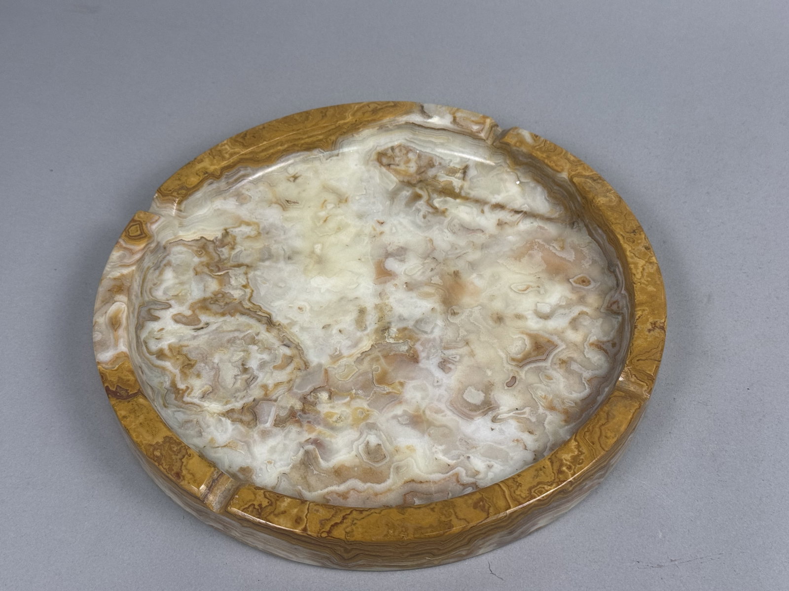 Large Vintage Banded Onyx Ashtray: A large Mid-Century Modern circular ashtray carved from polished banded onyx. The stone displays natural concentric and swirled patterns in tones of cream, amber, and dark brown. It features three