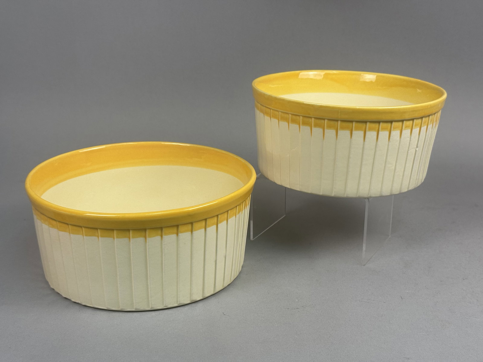 Pair of USA Ceramic Ovenware Bowls: This pair of graduated earthenware ovenware bowls features a vibrant yellow interior glaze and a cream-white fluted exterior. The round, straight-sided forms are marked on the base with USA OVENWARE,