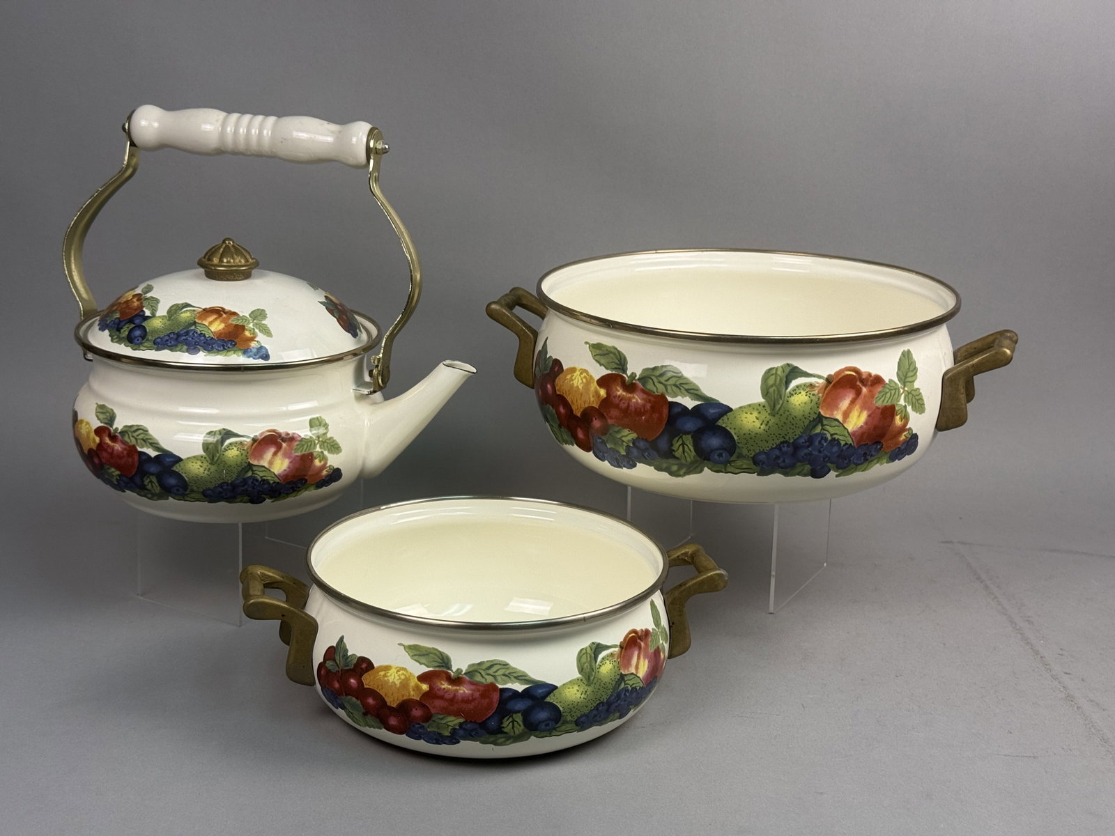 Trio of Lincoware Orchard Royale Cookware: This Lincoware Orchard Royale enamelware collection features a vibrant fruit motif and brass-tone hardware. The set includes a teakettle with a ceramic handle grip and two double-handle casserole
