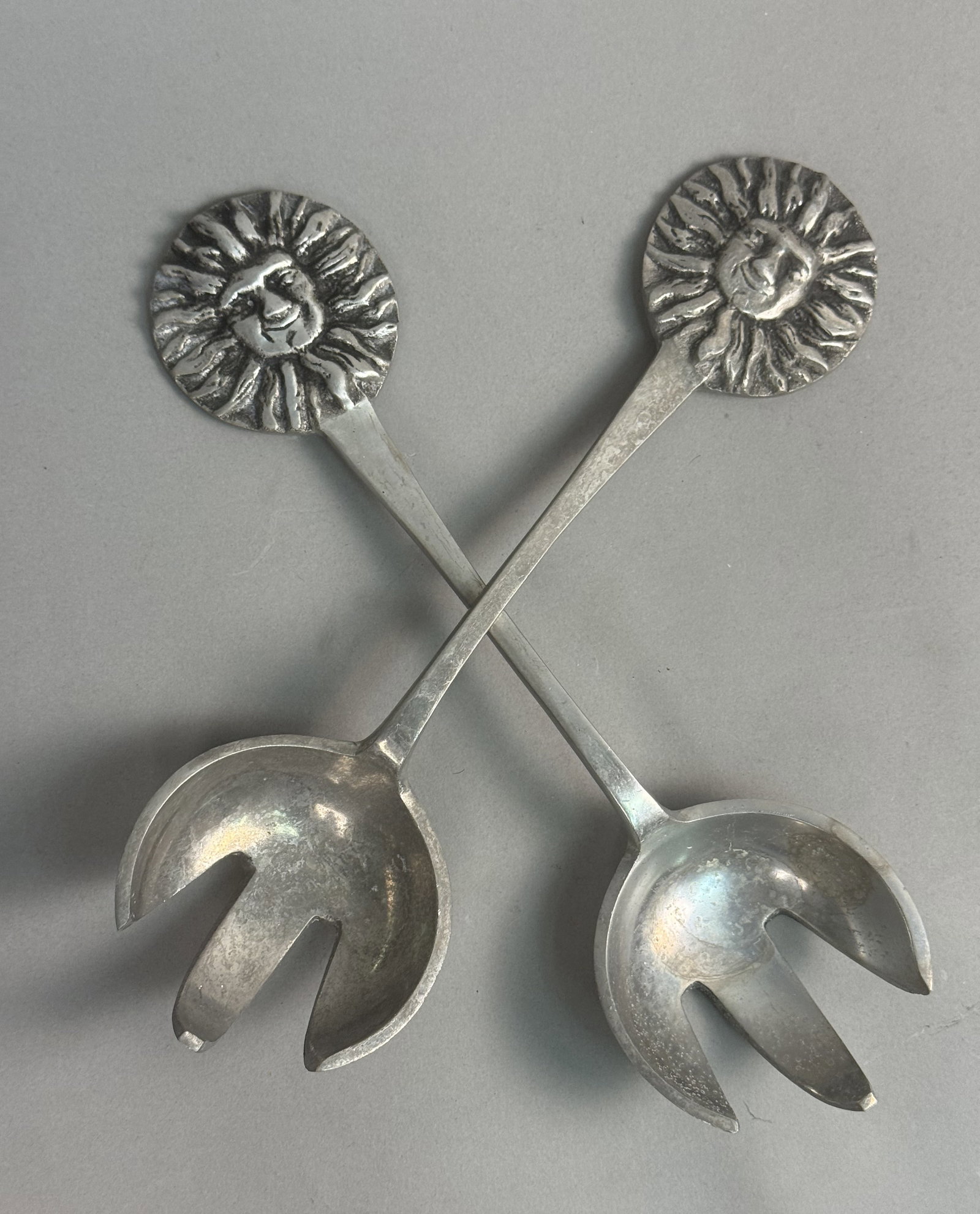 Mariposa Aluminum Sun Salad Servers: A pair of Mariposa sand-cast aluminum salad servers featuring anthropomorphic sun designs. Each server consists of a long handle with a circular finial depicting a smiling sun face and terminates in
