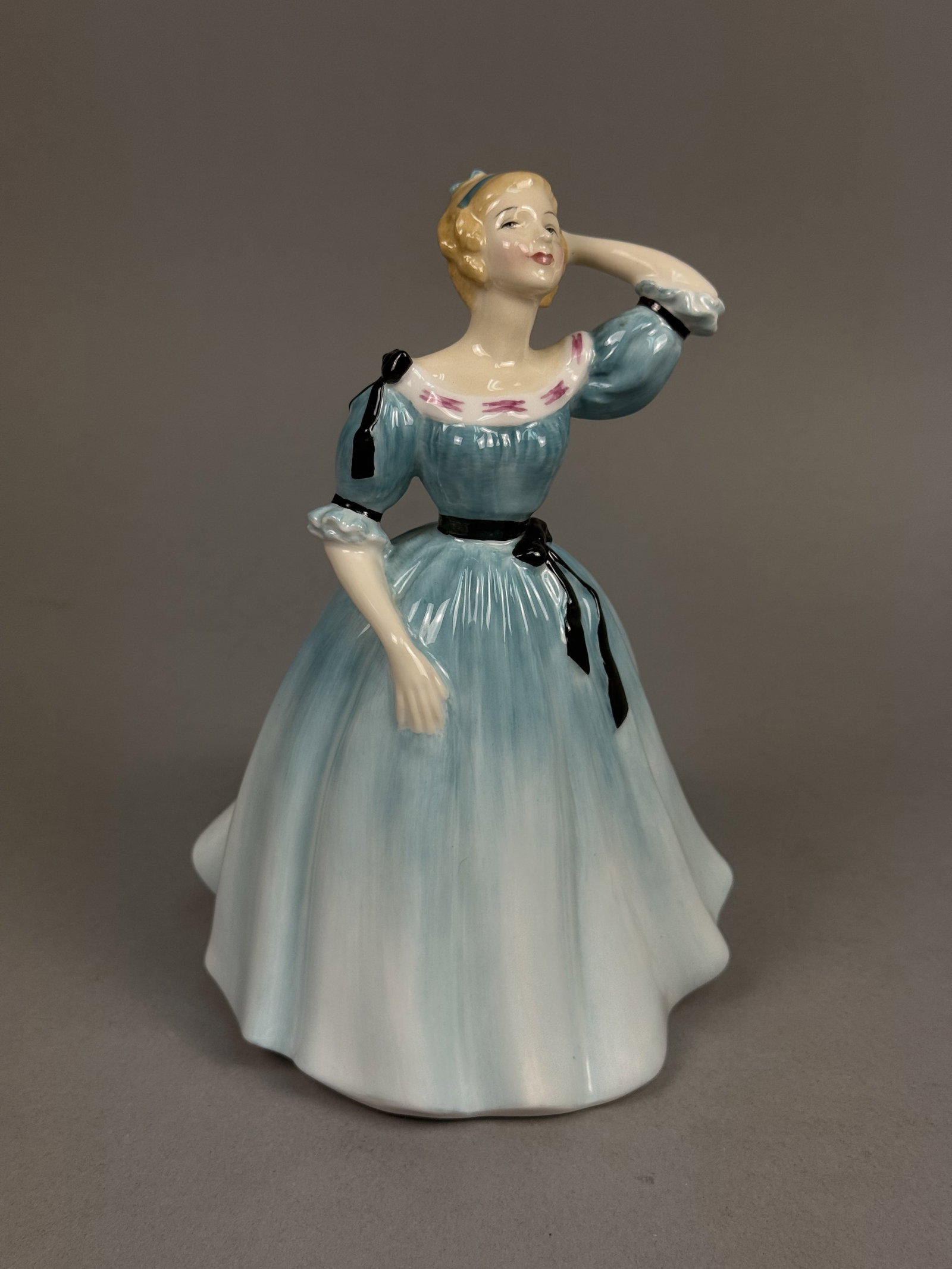 Royal Doulton Celeste Figurine HN 2237: This Royal Doulton bone china figurine, titled Celeste (HN 2237), is modeled with a raised left arm and finished with a hand-painted polychrome glaze. The figure wears a light blue period-style gown f