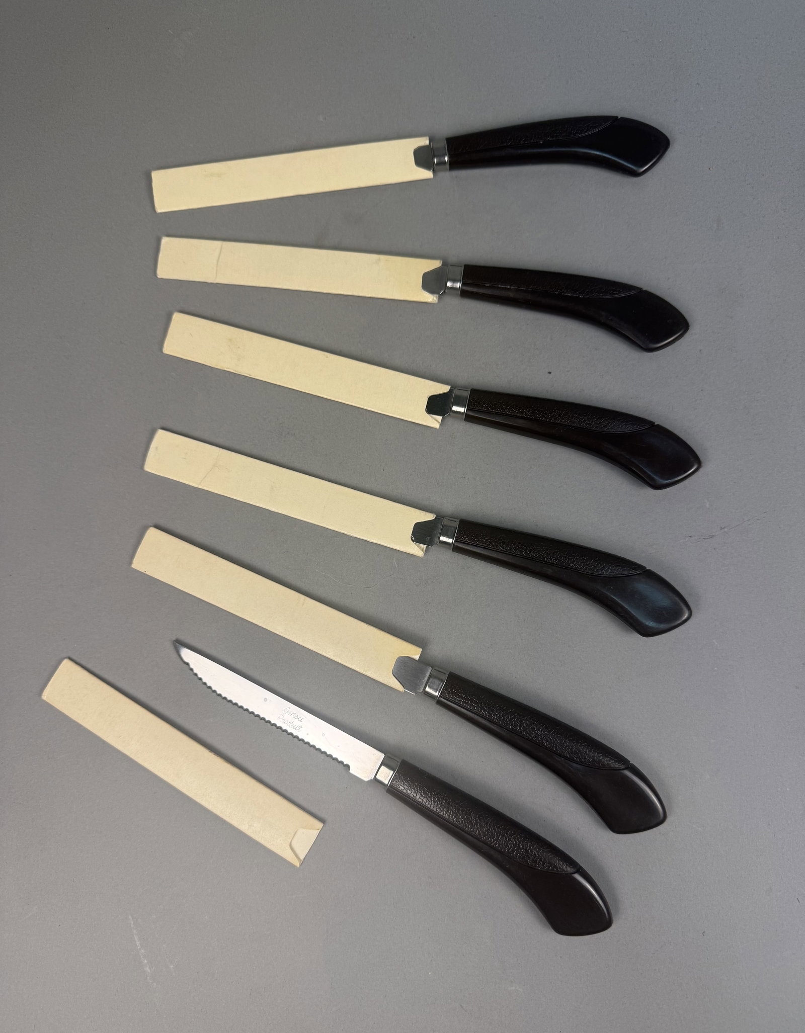 Set of Six Ginsu Steak Knives: This set of six Ginsu Product steak knives features stainless steel blades with full-length serrated edges. Each knife is constructed with a dark brown textured synthetic handle and a polished metal
