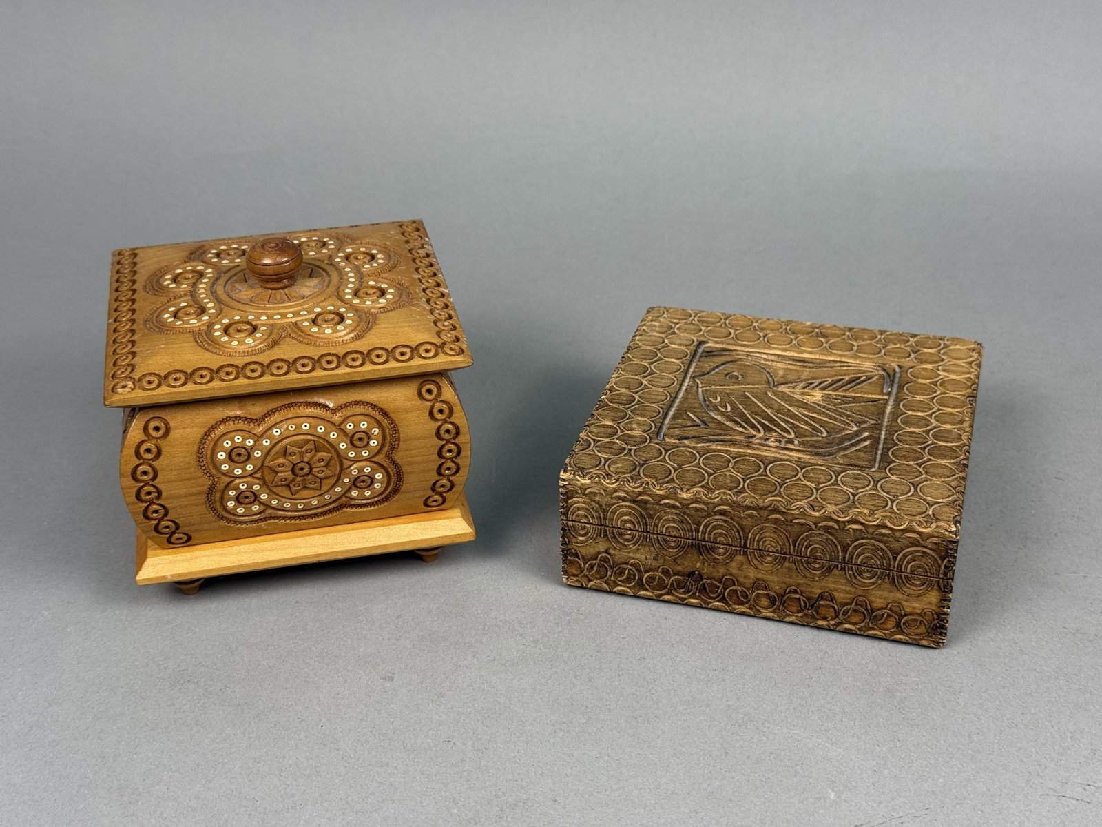 Two Carved Wood Trinket Boxes: Two wooden trinket boxes featuring traditional Eastern European folk art motifs. The footed box includes intricate chip-carving with circular inlays and bears a label reading Made in Ukraine on the