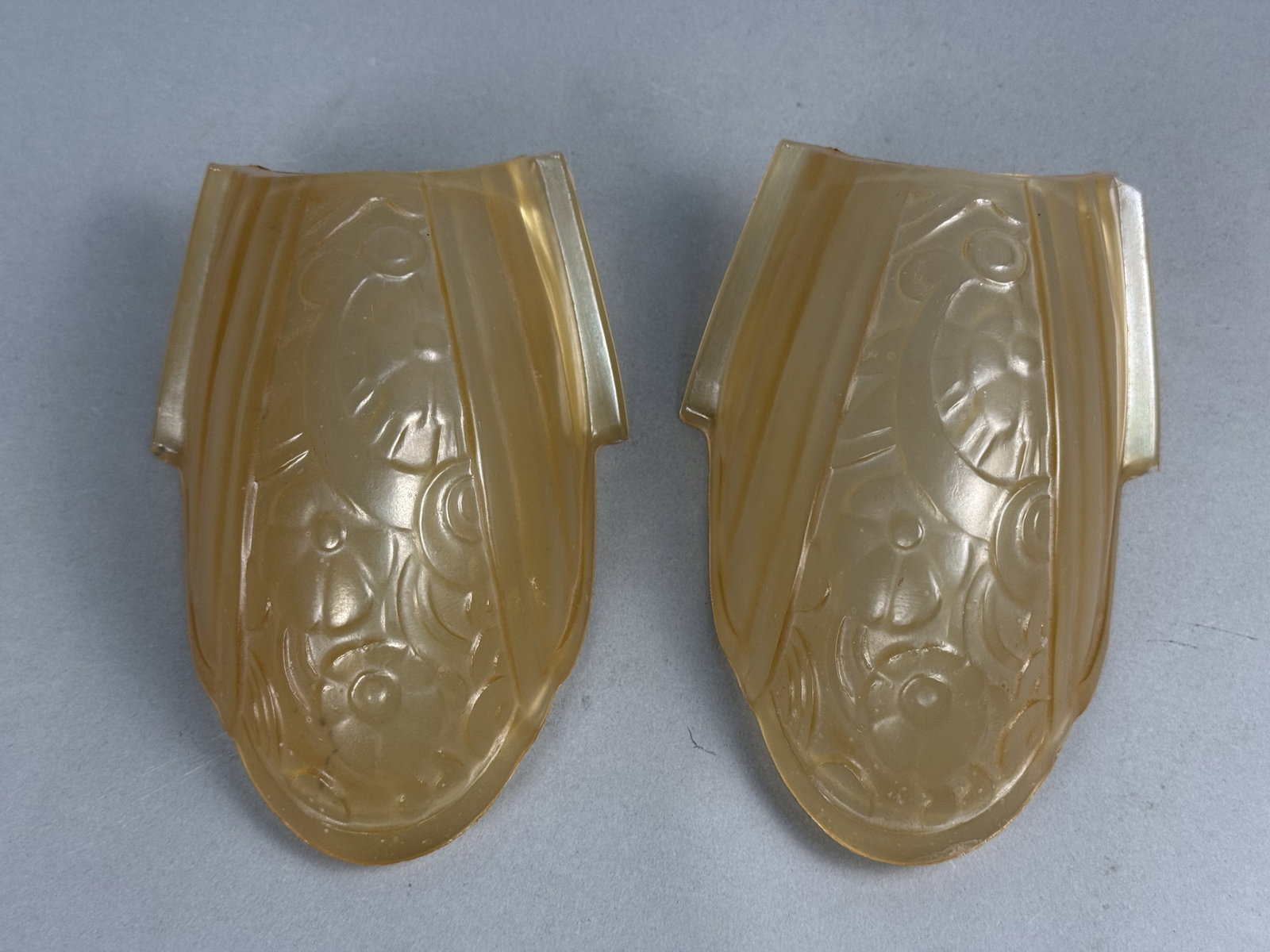 Pair of Lincoln Fleurette Slip Shades: A matching pair of Lincoln Fleurette pattern Art Deco slip shades molded in honey-amber glass with a frosted exterior finish. Each shade features a central relief-molded floral design accented by