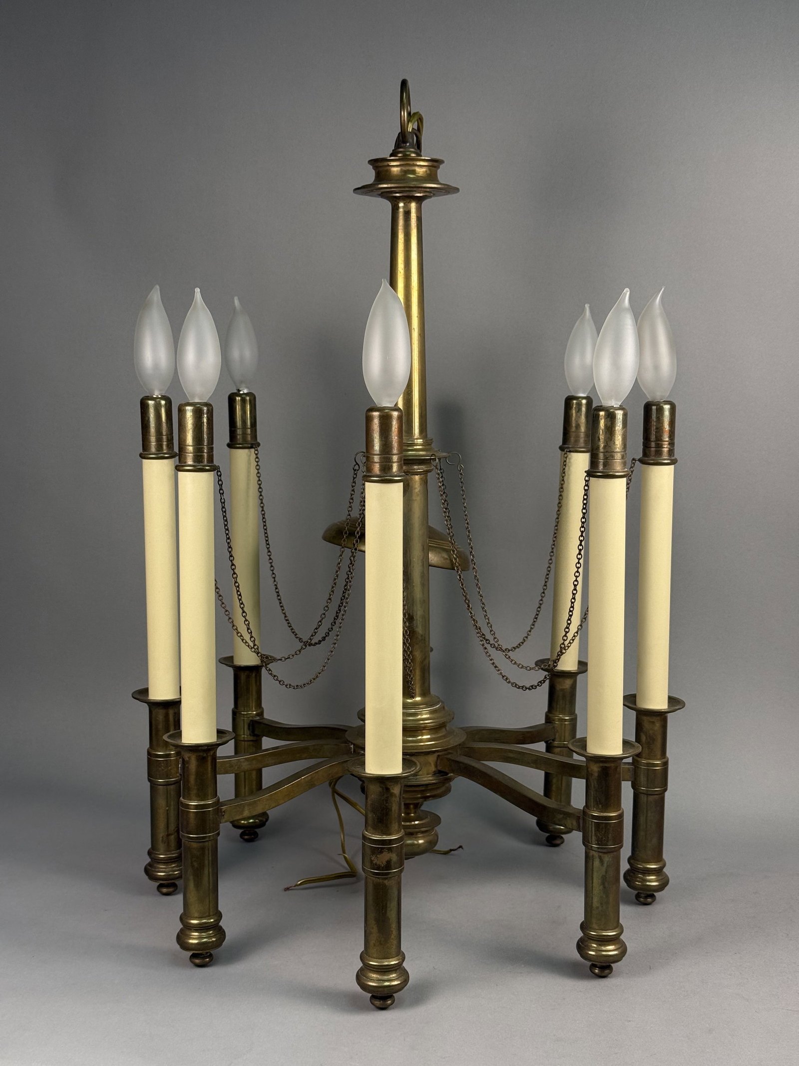 Chapman Brass Eight-Light Chandelier: A Chapman Mid Century solid brass eight-light chandelier featuring a central turned column and decorative chain swags. The fixture supports eight arms ending in candle cups with plastic sleeves and