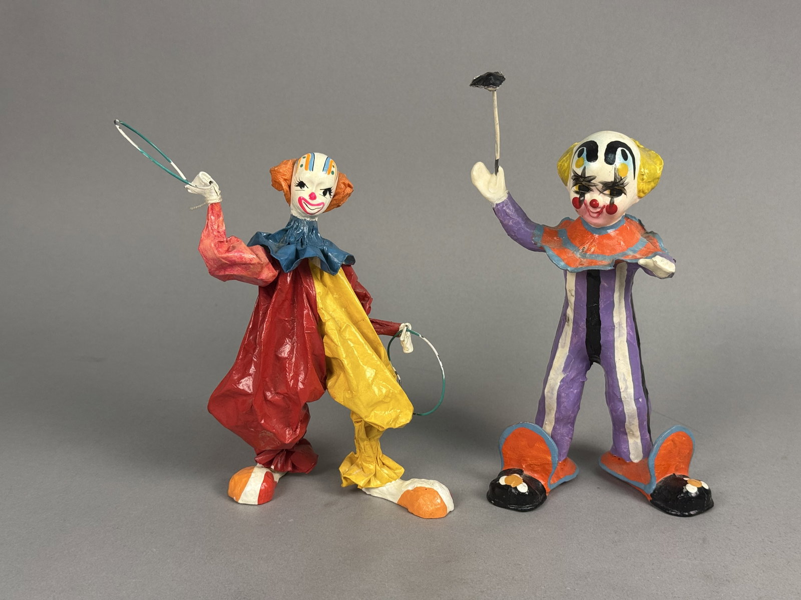 A Pair of Mexican Paper-Mache Clowns: A pair of hand-painted paper-mache folk art figurines from Mexico depicting acrobatic clowns. Each figure is constructed over a wire armature and decorated with colorful jumpsuits, ruffled collars,