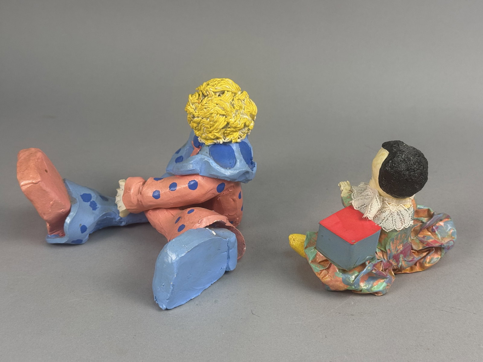 Two Hand-Painted Folk Art Clown Figurines: This lot comprises two vintage hand-crafted clown figurines including a larger molded composition figure and a smaller mixed-media Pierrot-style figure. The larger clown is depicted seated in a