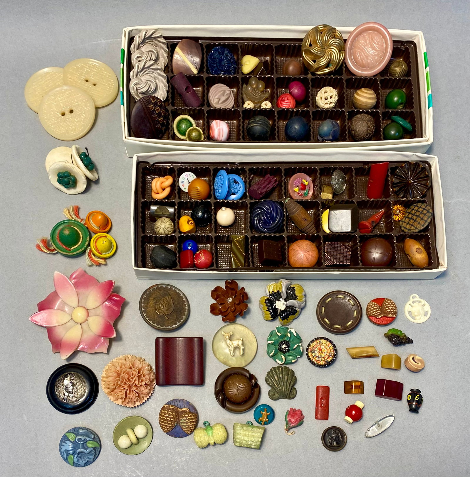 Assortment of Vintage Early Plastic Buttons: An assortment of 100 vintage buttons featuring early plastics including Bakelite, celluloid, and Lucite alongside wood and metal examples. The collection includes diverse novelty shapes such as a cloc