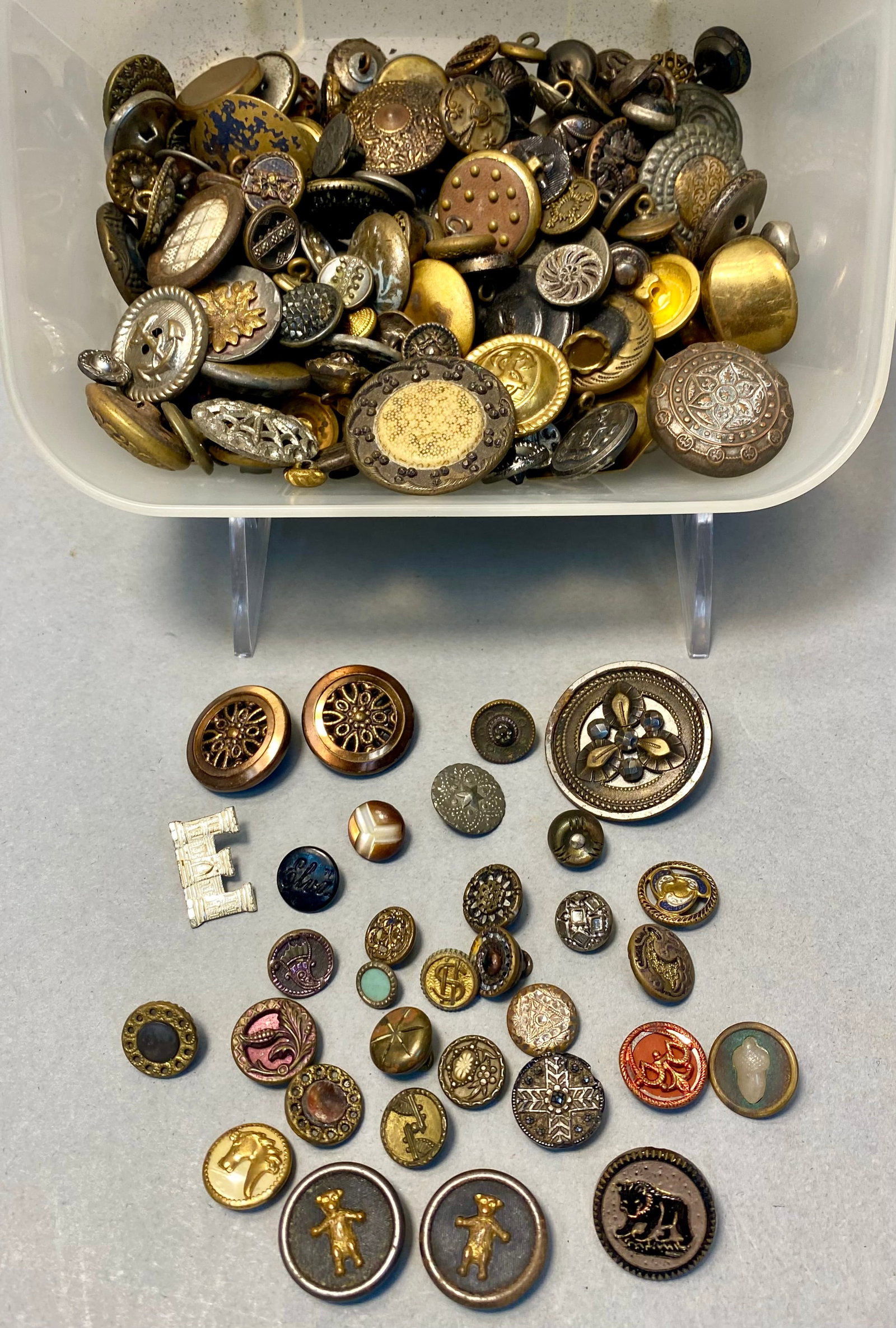 Assortment of Antique and Vintage Buttons: An assortment of vintage and antique buttons and pins featuring materials such as brass, silver-toned metal, mother-of-pearl, and molded glass. The collection includes various decorative motifs includ