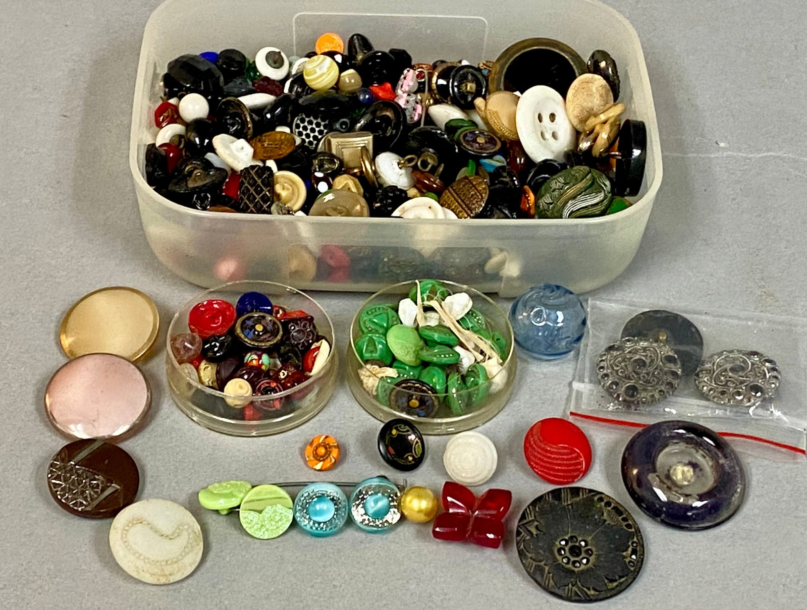 Collection of Vintage and Antique Buttons: An assortment of vintage and antique buttons composed of molded glass, metal, and early plastics in various colors and patterns. The group includes floral, geometric, and novelty shapes, such as a red
