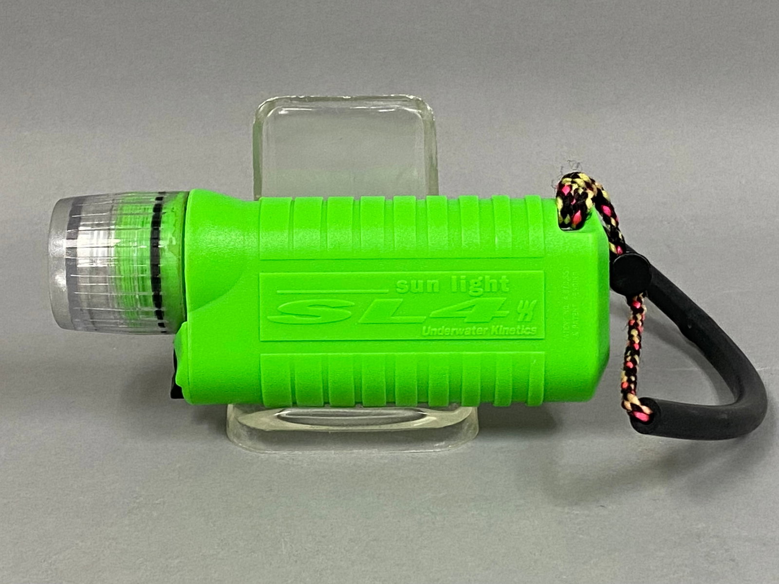 Underwater Kinetics SL4 Sun Light Dive Light: This Underwater Kinetics SL4 Sun Light handheld dive light features a high-visibility neon green plastic body and a clear, ribbed plastic bezel. The unit is equipped with a wrist lanyard consisting of