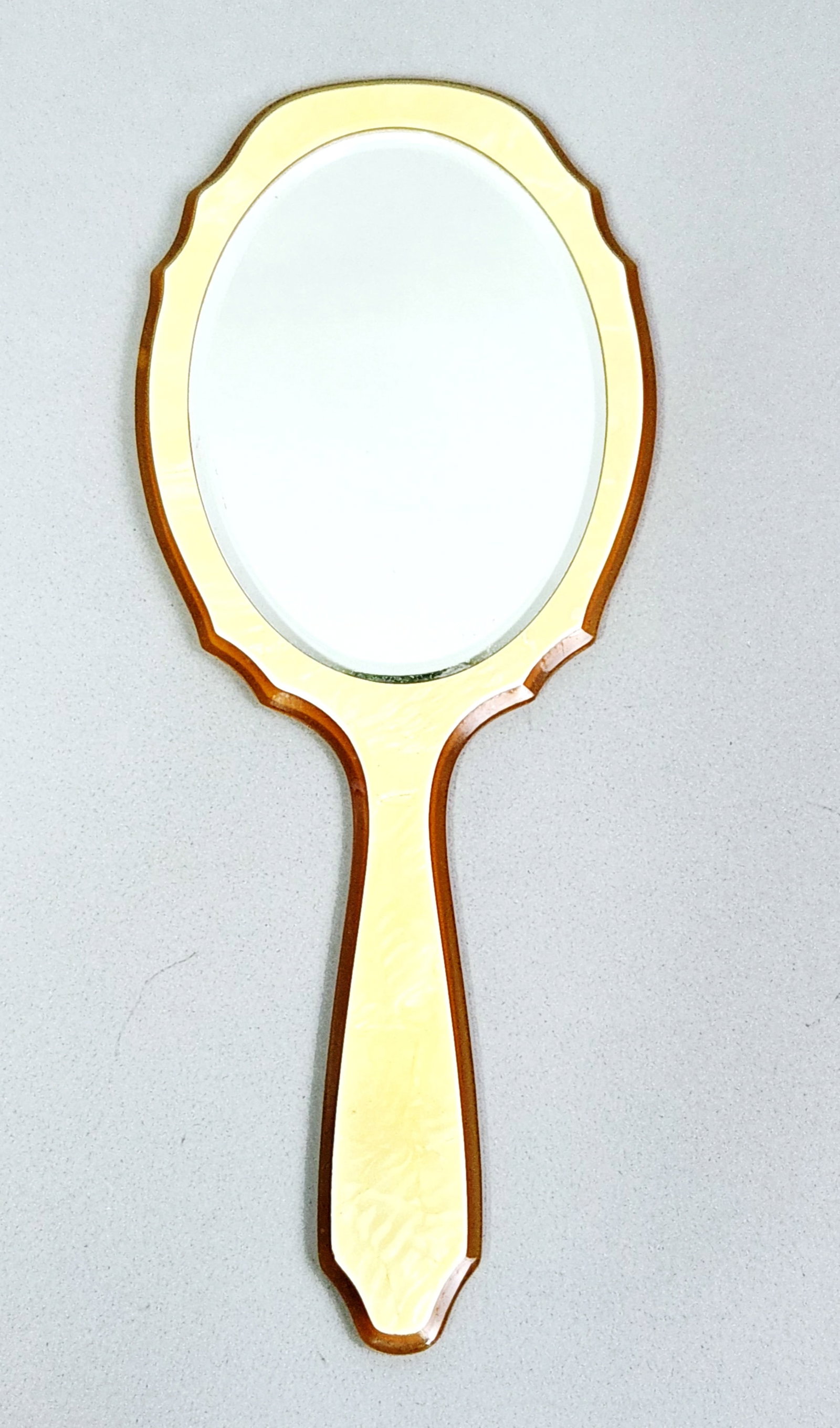 Vintage Pearloid & Celluloid Hand Mirror: A vintage handheld vanity mirror constructed from celluloid and pearloid early plastic. Length: 11.5 inches. Width: 5 inches. Visible internal crazing and fine surface cracks are present throughout th