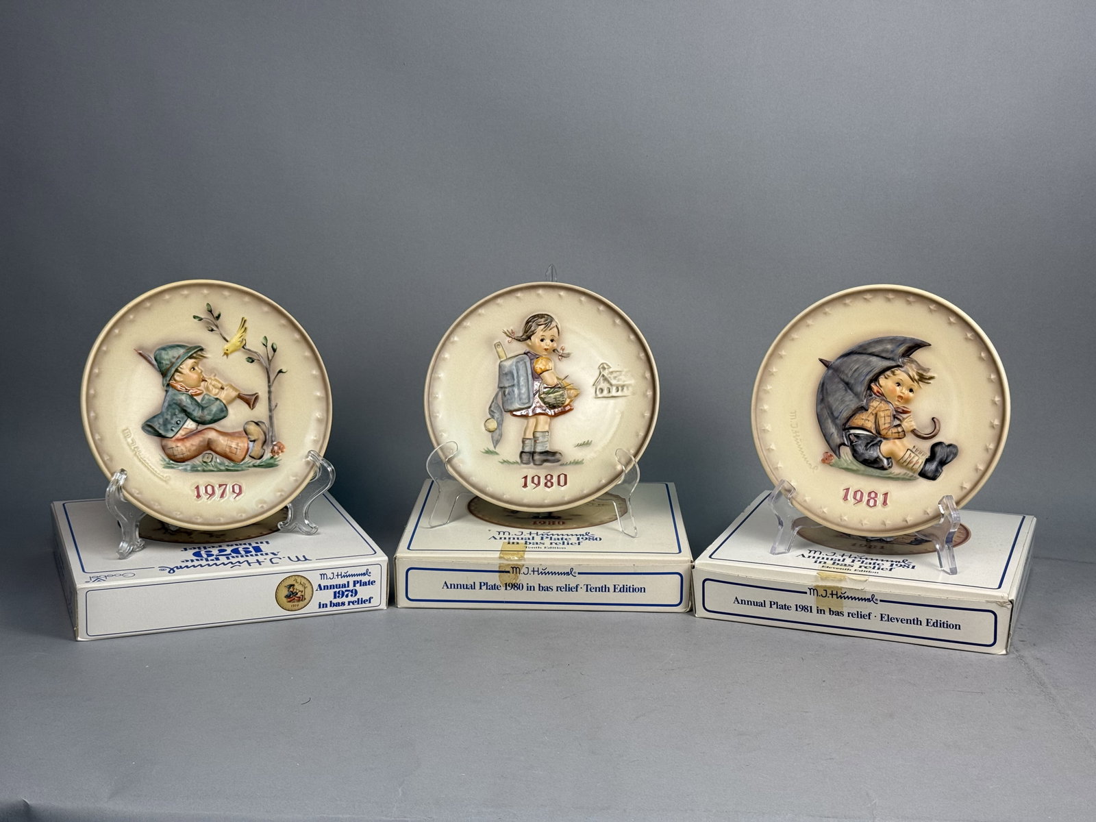 Three Goebel Hummel Annual Plates: A trio of Goebel M.J. Hummel annual collector plates for the years 1979, 1980, and 1981, featuring hand-painted bas-relief porcelain decoration. Each plate is marked on the reverse with the Goebel tra