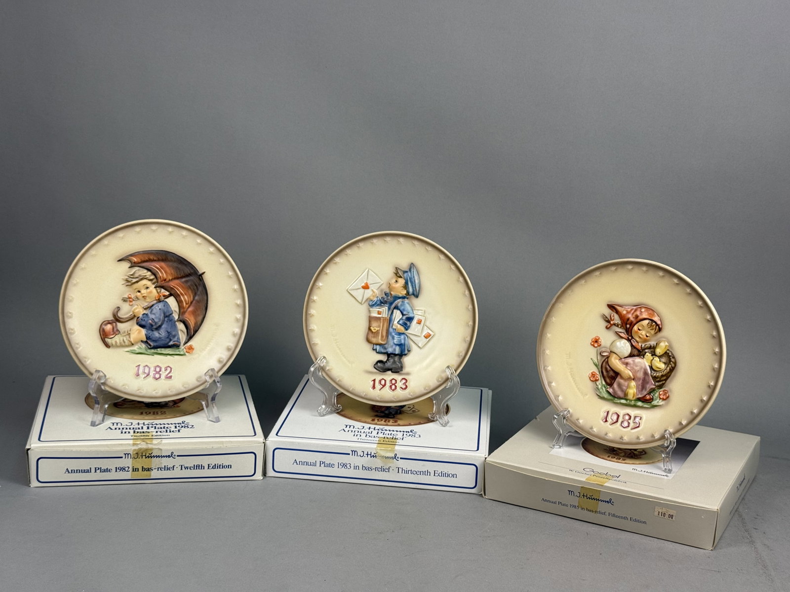 Three Goebel M.J. Hummel Annual Plates: Three porcelain collector plates by Goebel featuring bas-relief designs based on the artwork of M.J. Hummel. The set includes Twelfth, Thirteenth, and Fifteenth editions for the years 1982, 1983, and 