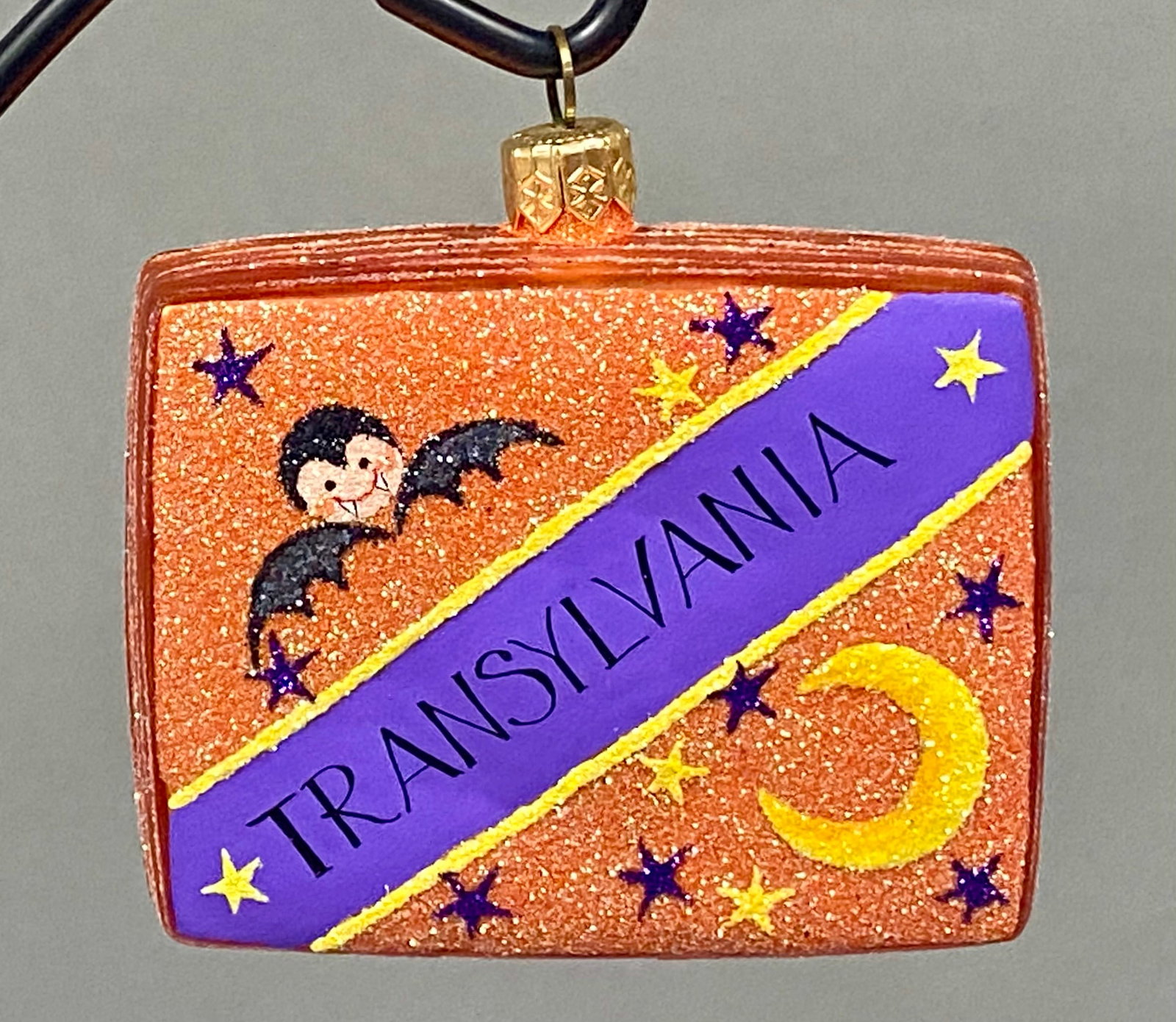 Christopher Radko Transylvania Halloween Ornament: A glass Halloween ornament, from Radko's "Transylvania State Fair" series, molded in the form of a postcard. The glittered front panel features a TRANSYLVANIA banner with a bat and celestial motifs, w