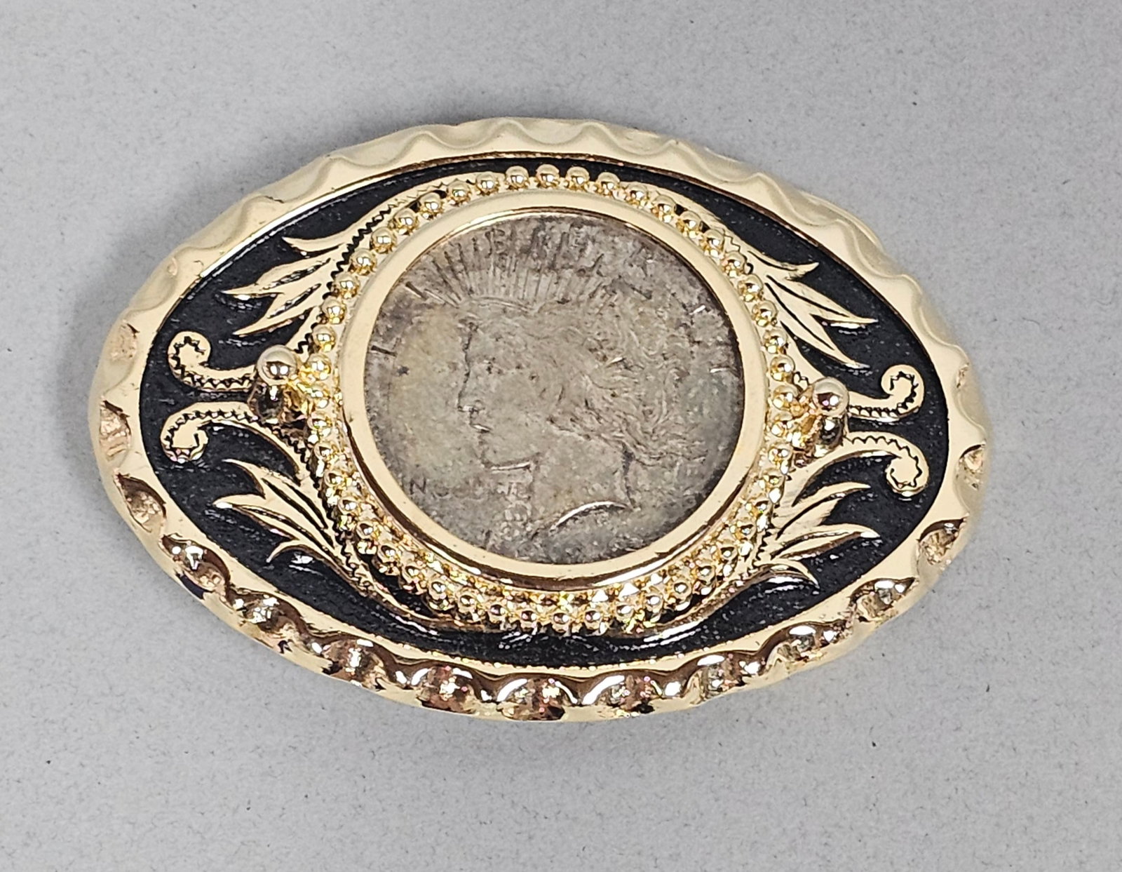 Western Peace Silver Dollar Belt Buckle: This oval western-style belt buckle features a genuine 1922 United States Peace Silver Dollar set within a beaded gold-tone bezel. The gold-plated base metal frame is accented with black enamel