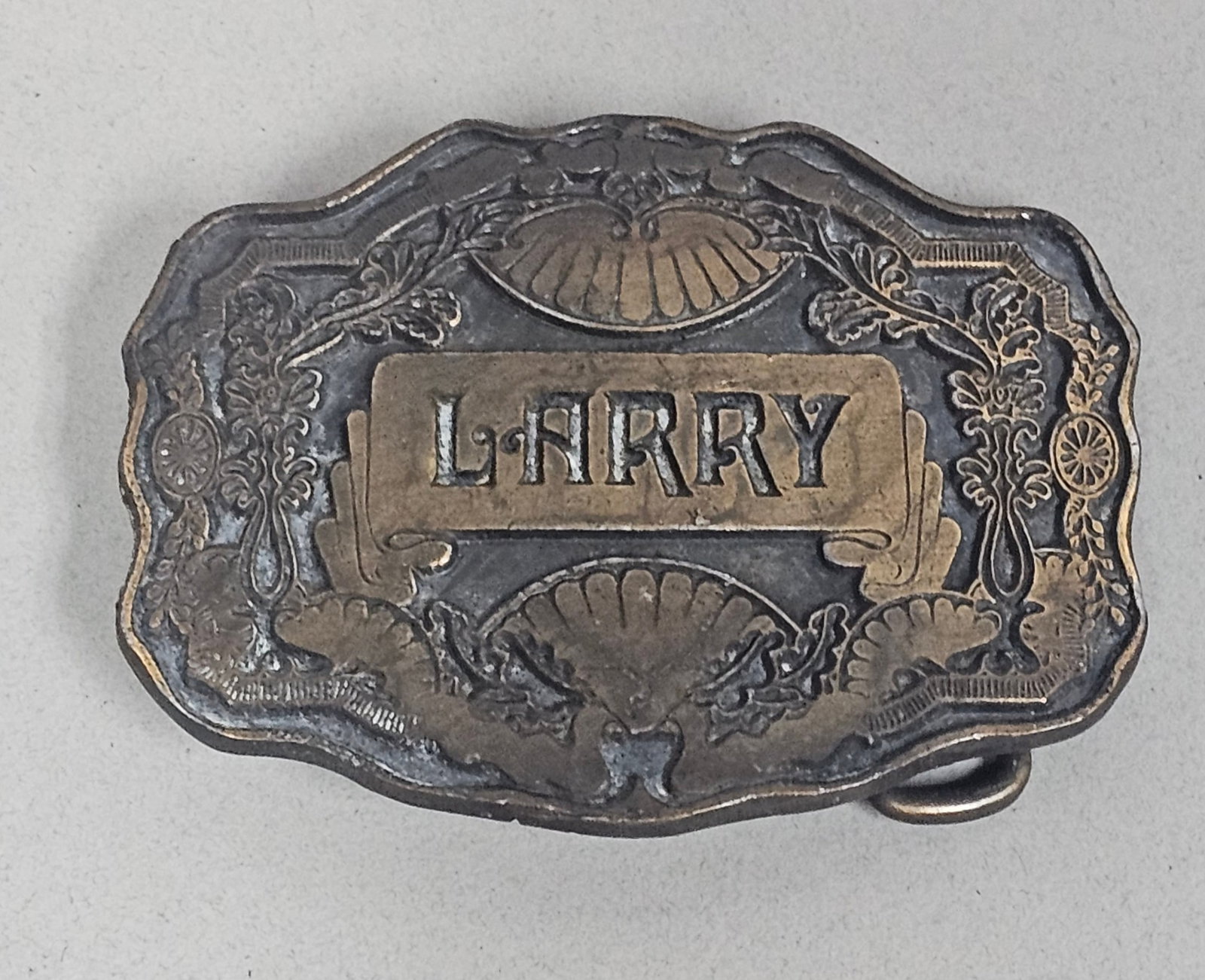 Vintage Personalized Larry Belt Buckle: This personalized cast metal belt buckle features the name Larry in raised block letters on a central rectangular plaque. The ornate frame includes lobed scalloped edges decorated with shell motifs