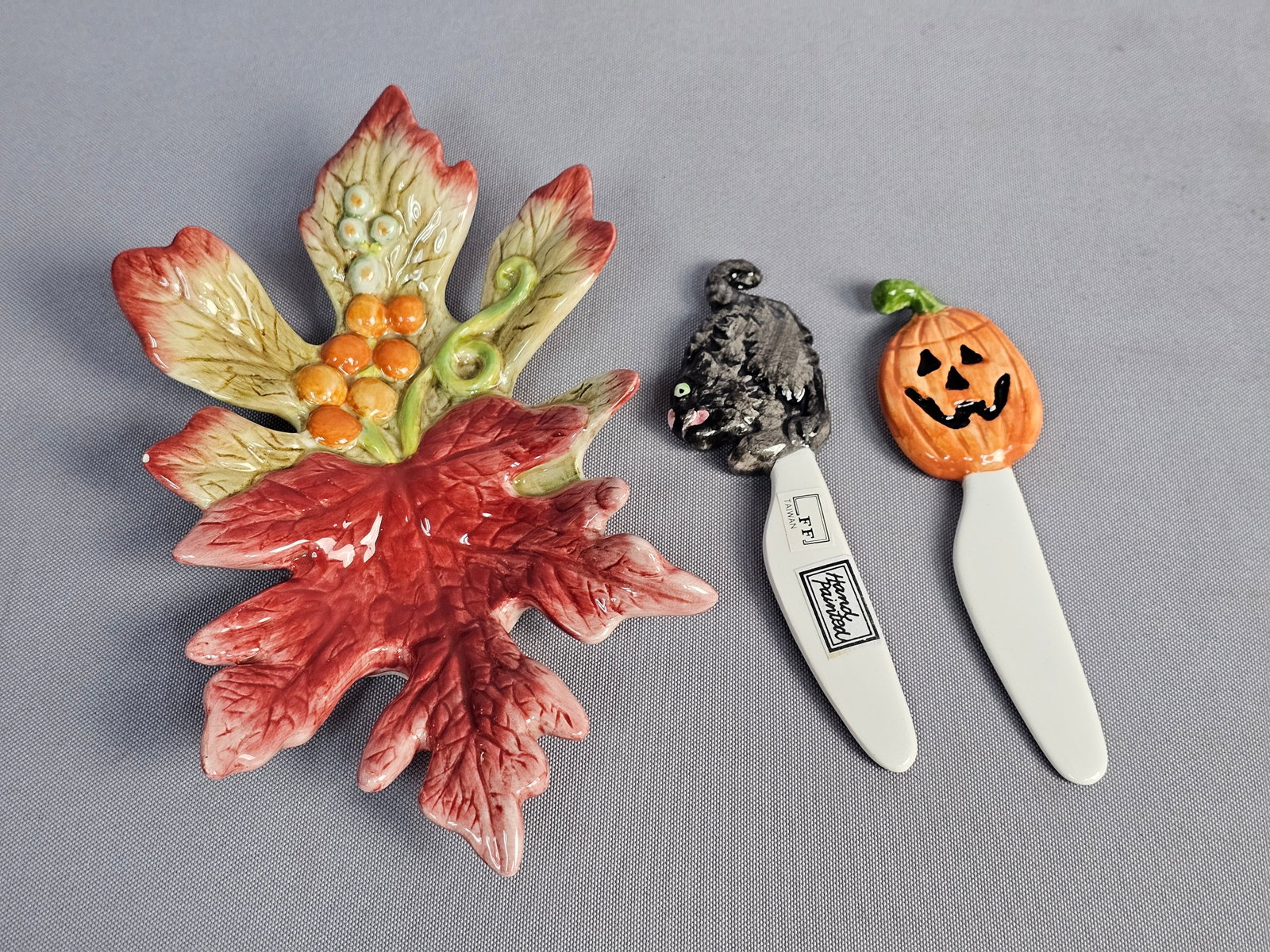 Three Fitz and Floyd Seasonal Ceramics: Three Fitz and Floyd hand-painted ceramic items including an Autumn Fields pattern leaf dish and two Halloween-themed figural spreaders. The lot features a multi-lobed leaf dish with dimensional