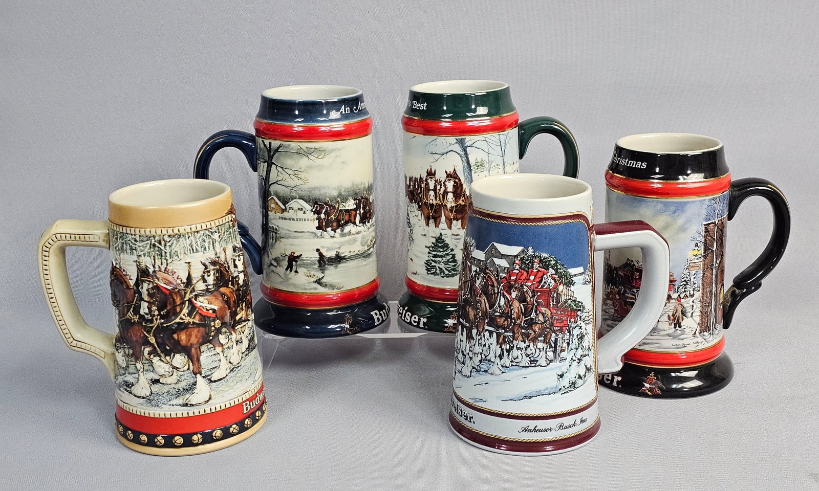 Set of 5 Budweiser Holiday Steins: This set of five glazed ceramic commemorative steins was produced by Ceramarte for Anheuser-Busch between 1988 and 1992. The collection features wrap-around transfer prints and high-relief molded