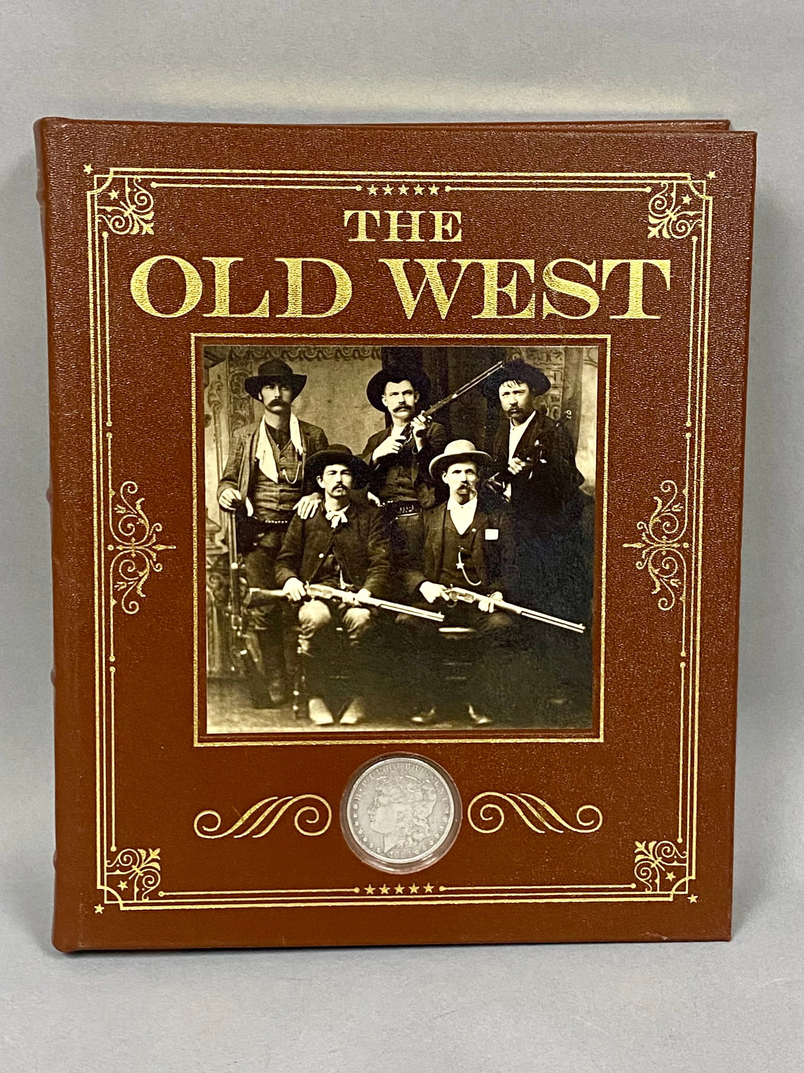 Hyslop. The Old West. National Geographic.: This deluxe quarto edition is bound in brown pebbled leatherette featuring ornate gilt-stamped scrollwork and an 1885 Morgan Silver Dollar inset into the front cover. The volume is profusely illustrat