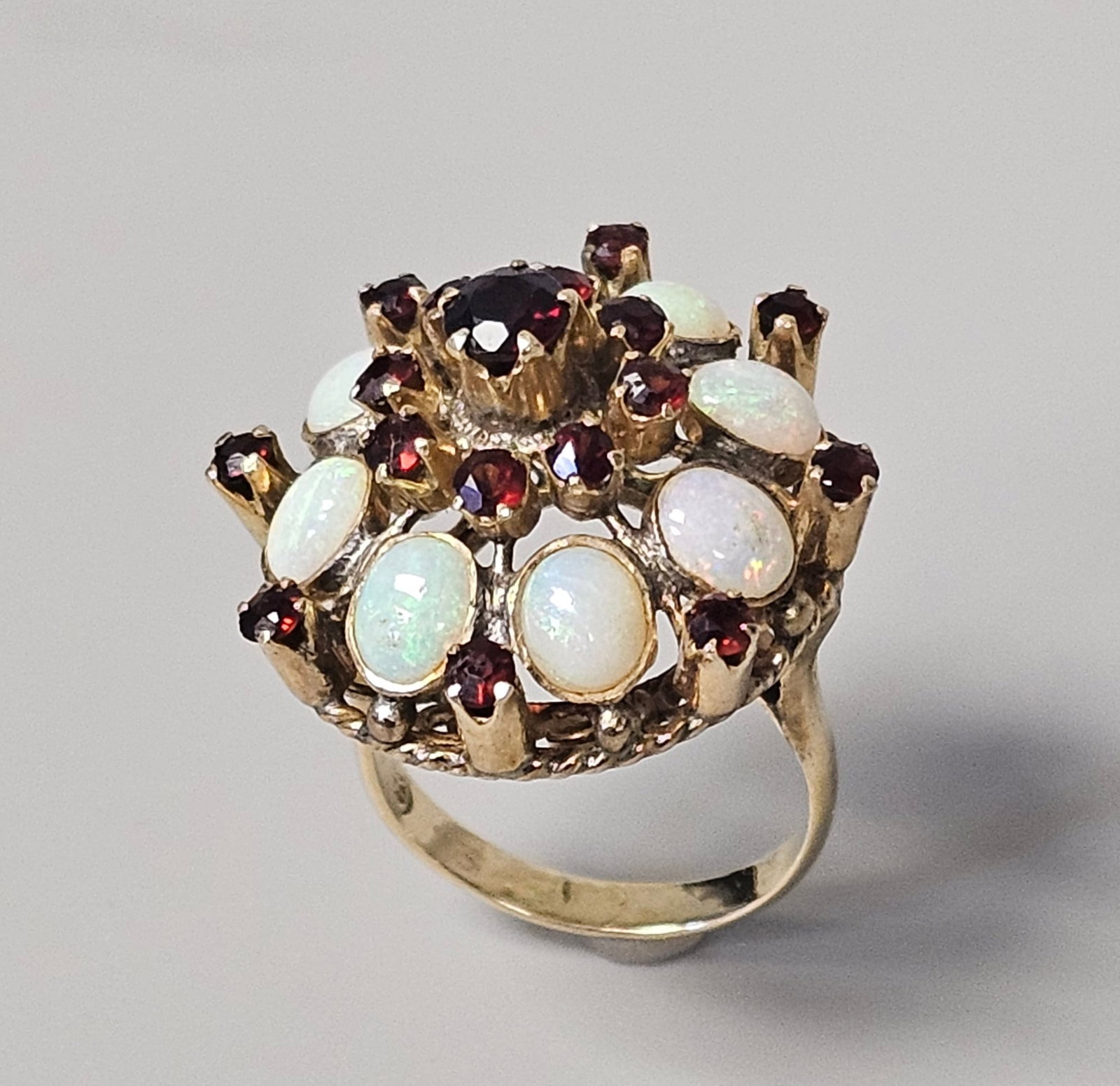 14K Gold Opal Garnet Princess Ring 7.4 Grams: This vintage size 6 cocktail ring features a high-profile tiered dome setting in 14 karat yellow gold, weighing 7.4 grams. It is set with eight oval cabochon white opals displaying vibrant play-of-col