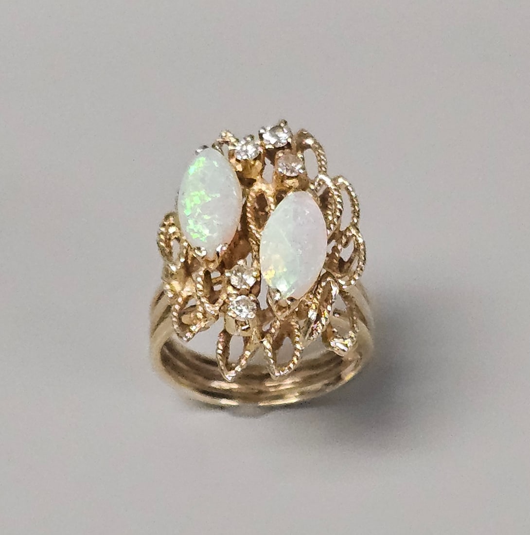 14K Gold Opal & Diamond Cocktail Ring 6.9 Grams: This 14 karat yellow gold ring features an elaborate textured openwork setting in a tiered sculptural design. Two marquise-cut white opals exhibiting a green and pink play-of-color are prong-set along