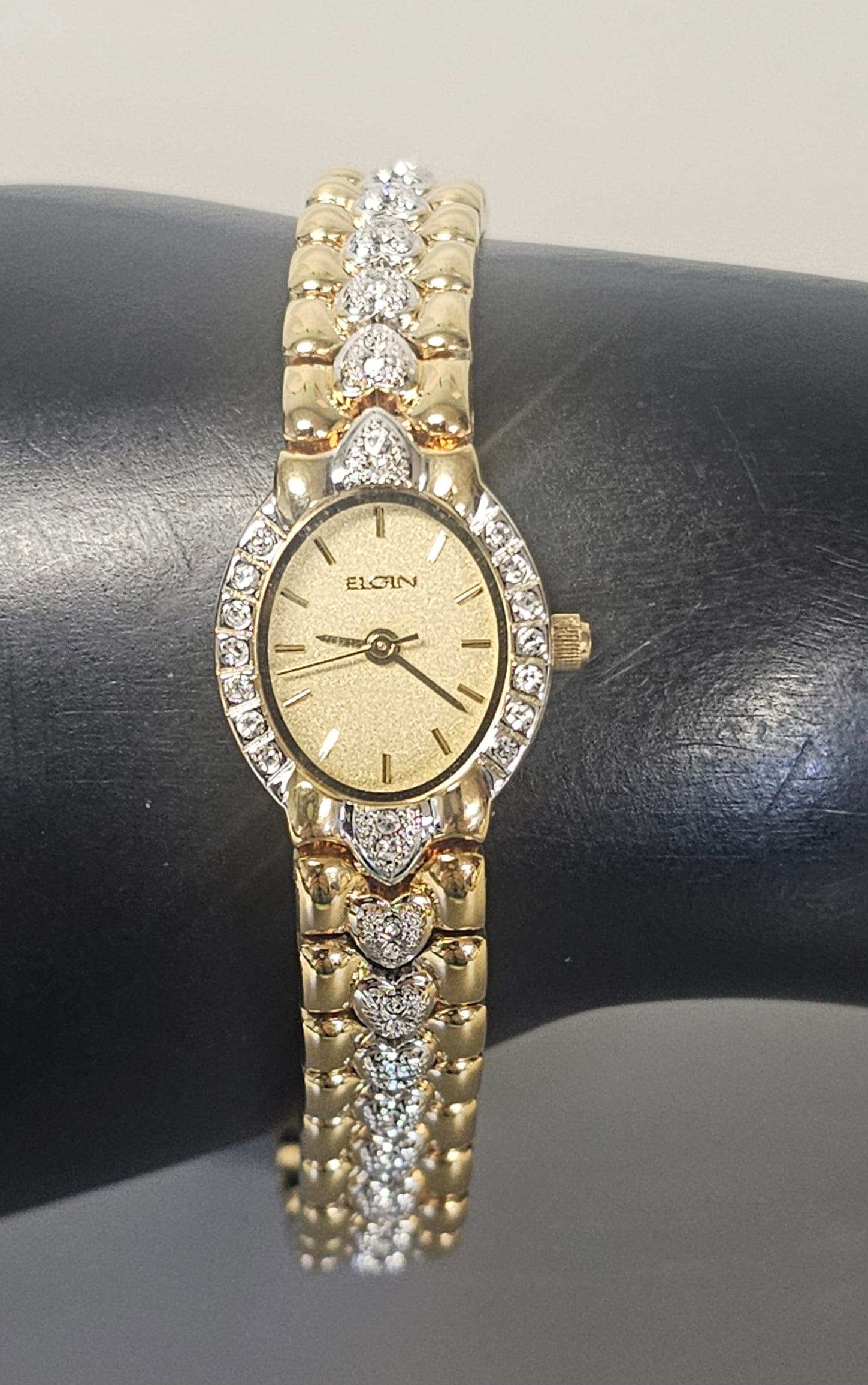 Two-Tone Elgin Heart-Link Watch: This ladies' Elgin quartz wristwatch features a textured gold-tone dial with applied baton markers and matching hands. Total length measures approximately 7.5 inches and the case measures 0.75 inches 