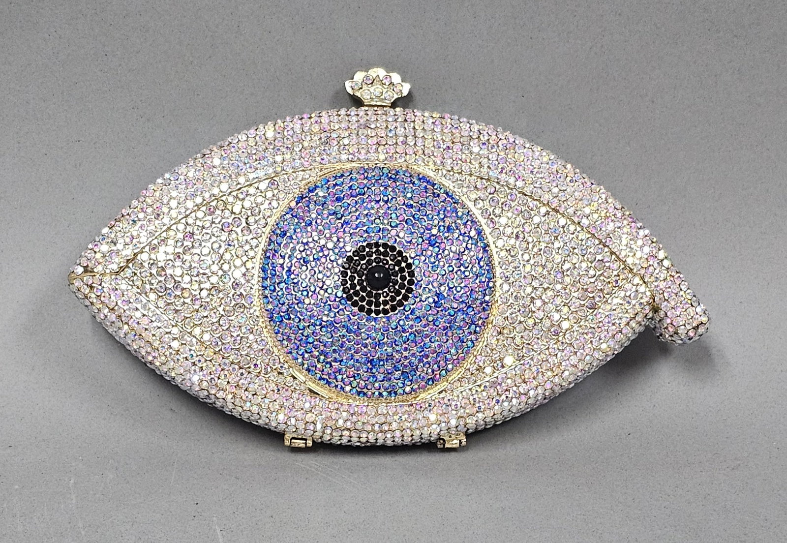 Rhinestone Evil Eye Novelty Clutch: A novelty minaudiere designed in the form of a stylized eye with a full pave set rhinestone exterior. The central iris features concentric rings of blue and iridescent purple crystals around a black p