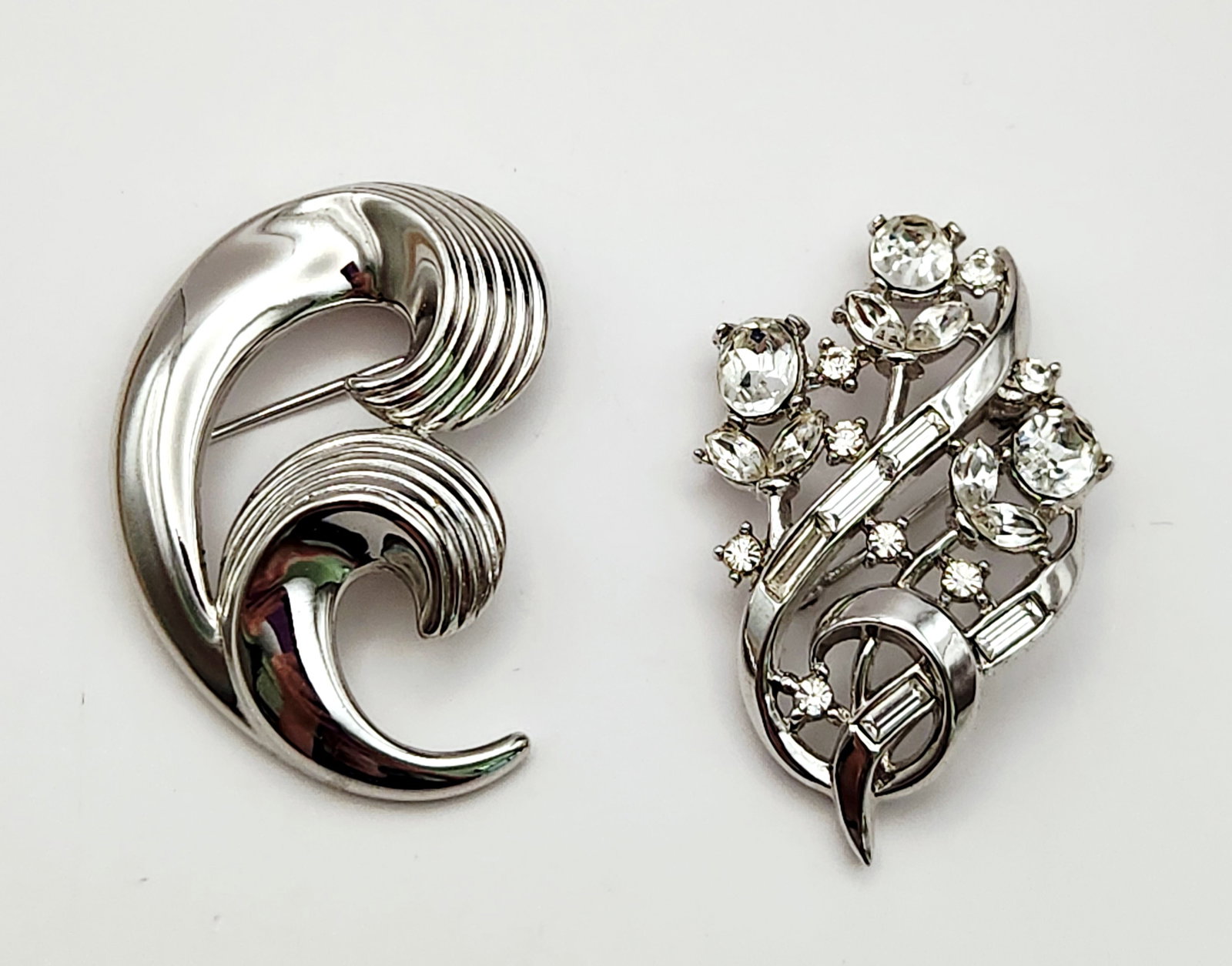 Vintage Trifari Brooches Pins: This lot consists of two mid-century silver-tone brooches produced by Trifari. Modernist brooch: 2 inches in length Floral brooch: 2 inches in length. Both pieces are in good vintage condition with