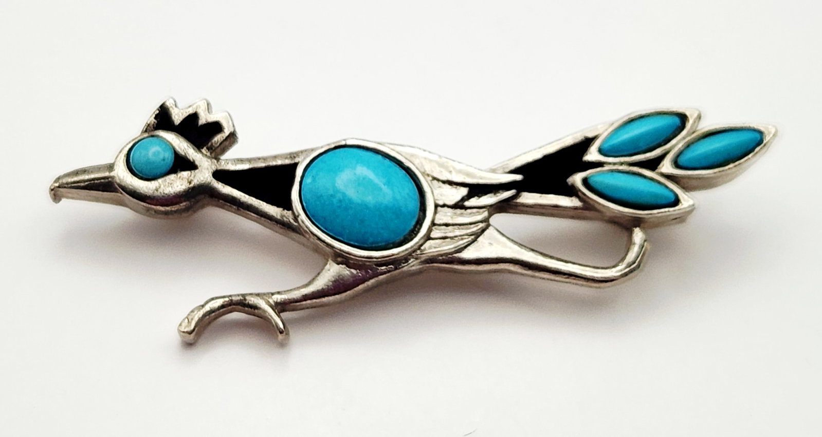 St. Labre Roadrunner Brooch: A silver-toned cast metal figural brooch by St. Labre depicting a roadrunner in a running profile. The design is set with five faux turquoise cabochons. Length: 2.25 inches (57 mm). The item is in