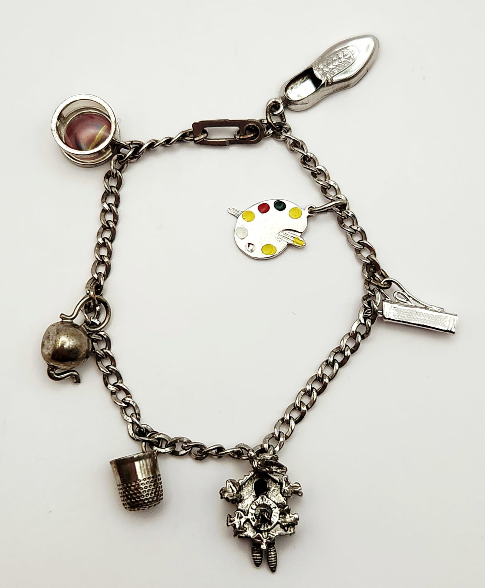 Vintage Charm Bracelet: A vintage silver tone curb link bracelet featuring seven assorted charms. Only 2 of the charms are marked sterling. Length: 7.5 inches. The bracelet displays significant tarnish and patina throughout