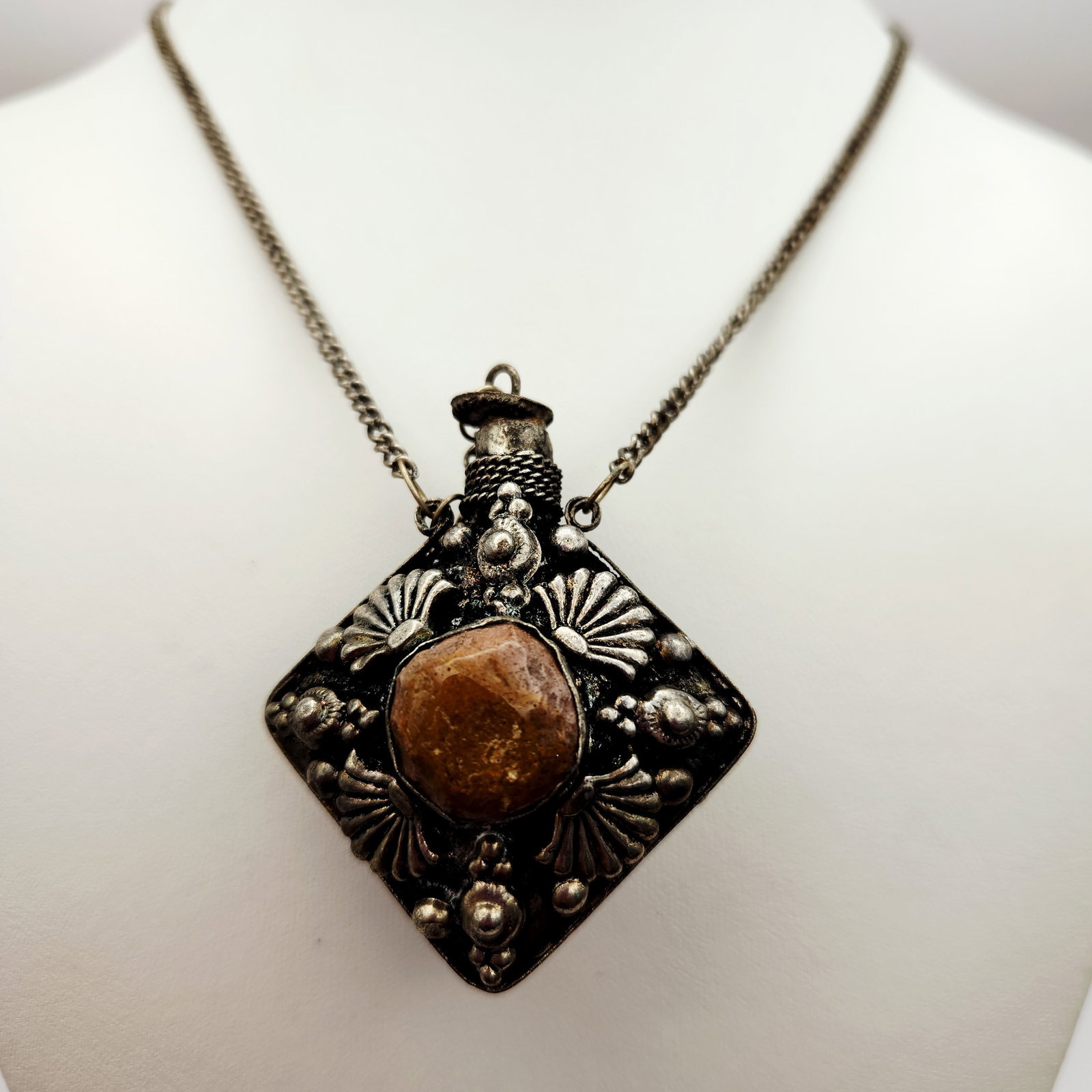 Vintage Silver-Tone Perfume Bottle Necklace: An ornate silver-tone perfume flacon pendant in a diamond orientation featuring elaborate repousse and filigree metalwork. The dual-sided design is set with a central green cabochon on one side and a 