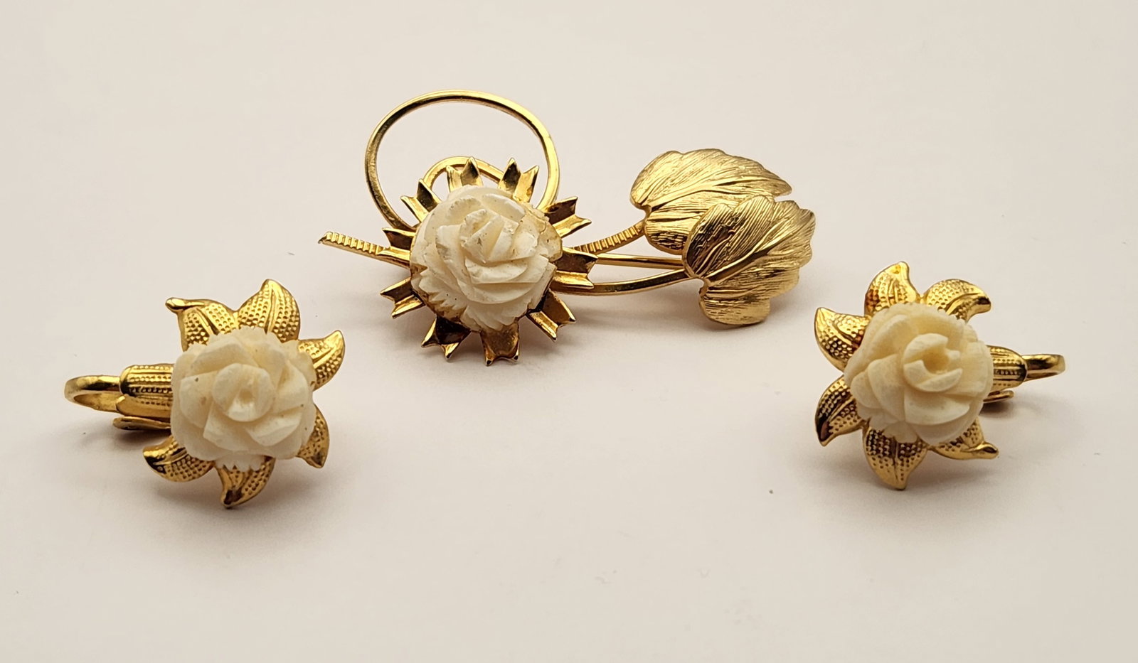 Carved Rose Jewelry Set: A yellow gold-tone brooch and a pair of matching clip-on earrings feature carved white roses. Brooch measures 1.75 inches long. Earrings measure 0.75 inches in diameter. The set is in good vintage