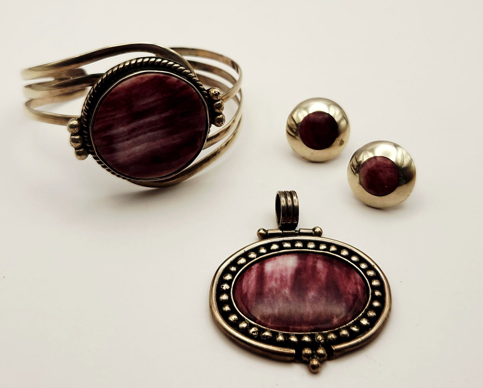 Silver Purple Spiny Oyster Suite: A jewelry suite comprising a cuff bracelet, a pendant, and a pair of stud earrings, each featuring bezel-set purple spiny oyster shell cabochons with natural banding. The earrings & pendant are