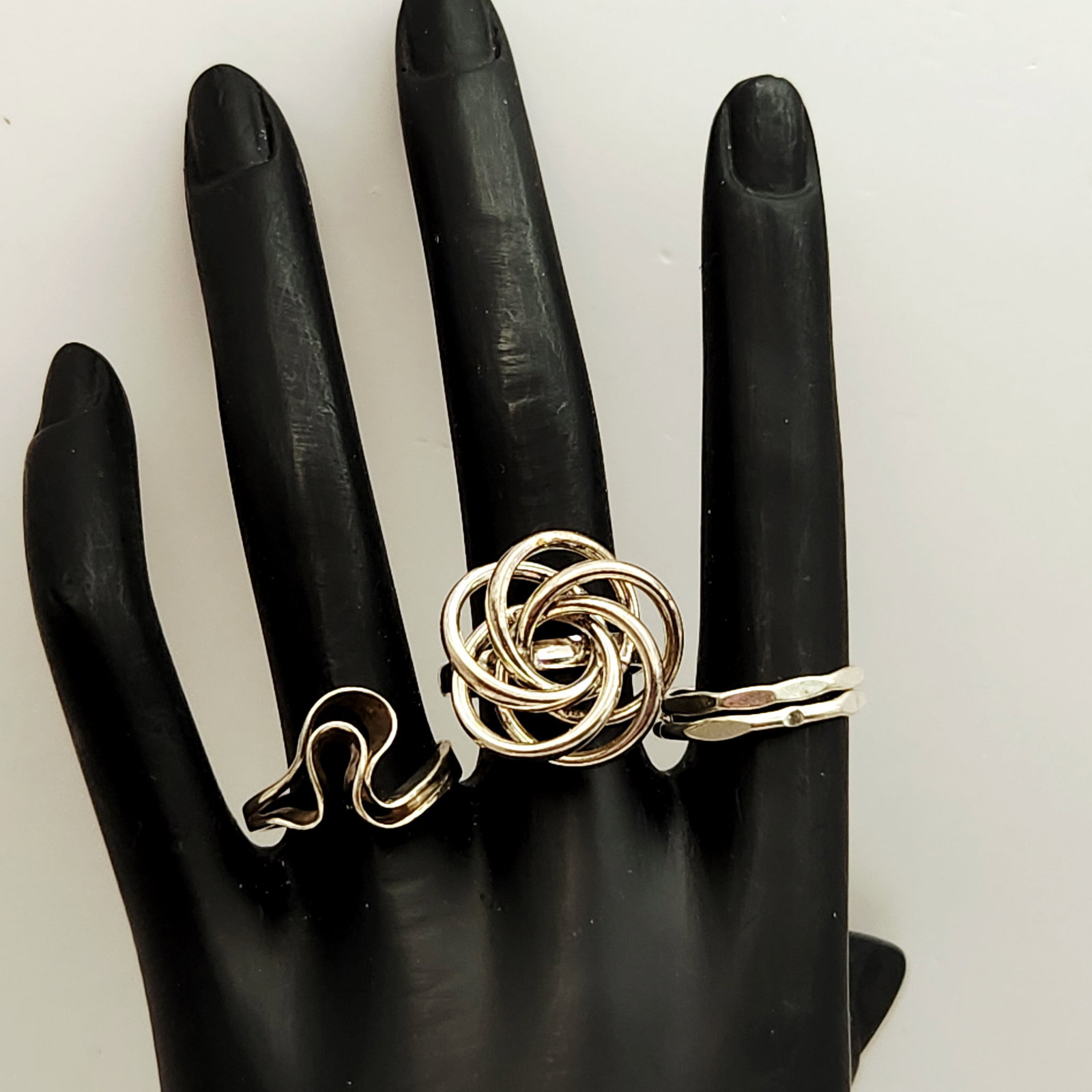 Sterling Modernist Rings 10.8 Grams: A trio of sterling silver rings featuring modernist sculptural designs, including an undulating wavy band, a multi-loop knot ring, and an interlinked double-band set with hammered textures. Sizes: 7,