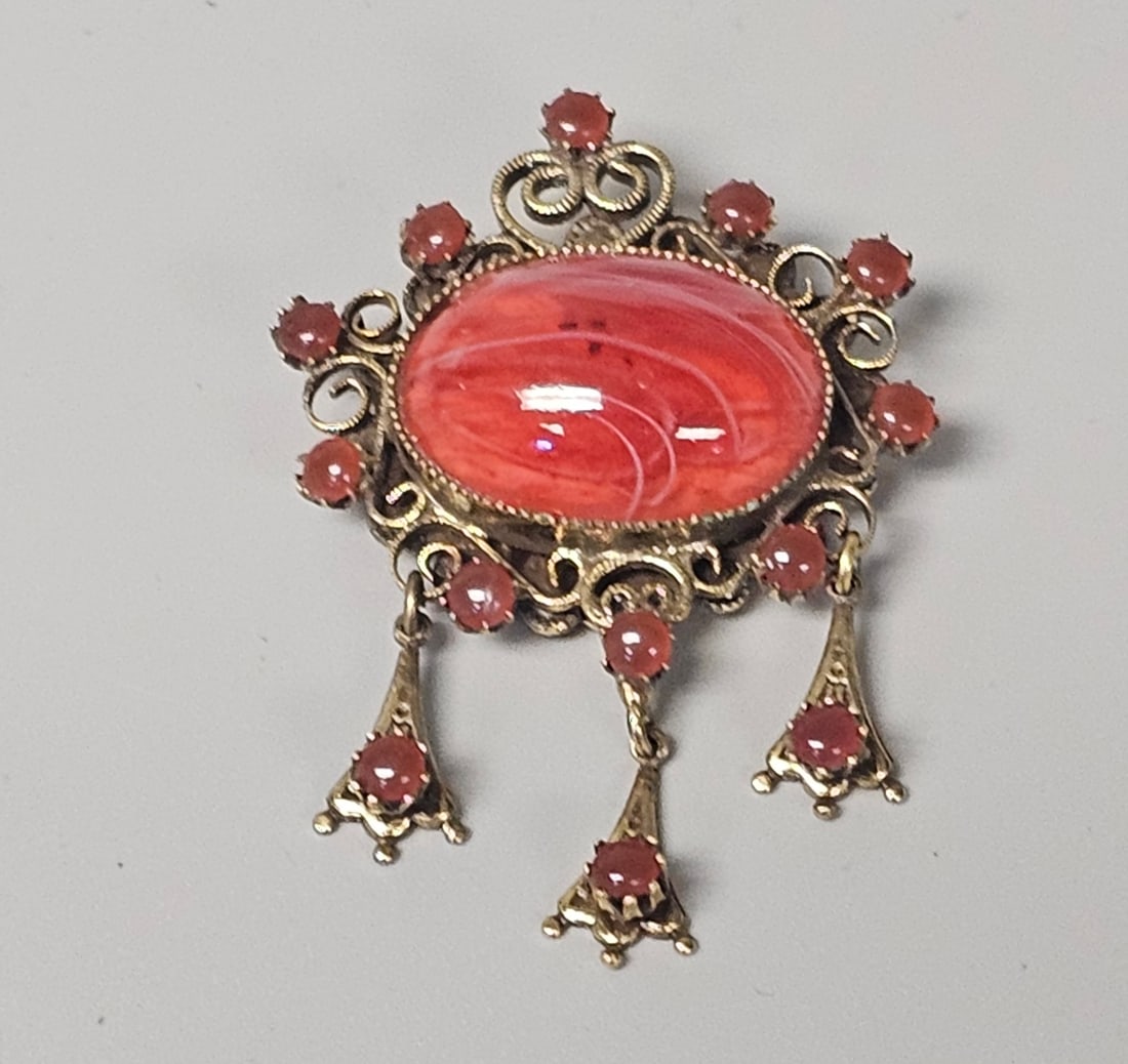 Original by Robert Glass Dangle Brooch: This Victorian-revival brooch features a gold-tone filigree frame set with a large red-and-white swirled art glass cabochon and multiple smaller reddish-orange glass cabochons. Across the widest