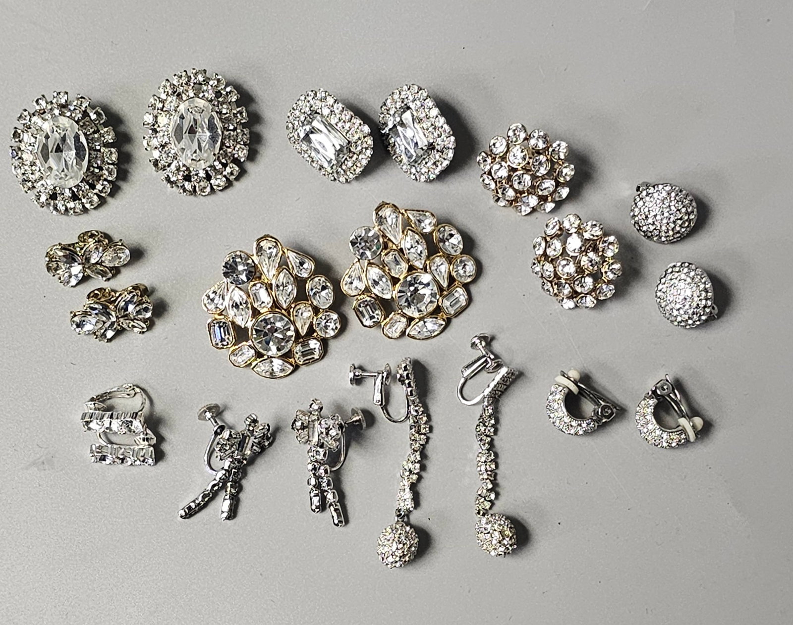 Collection of Vintage Rhinestone Earrings: An assortment of vintage costume jewelry earrings and one single fur clip. The collection features various mid-century cocktail styles including oval and rectangular clusters, floral motifs, and