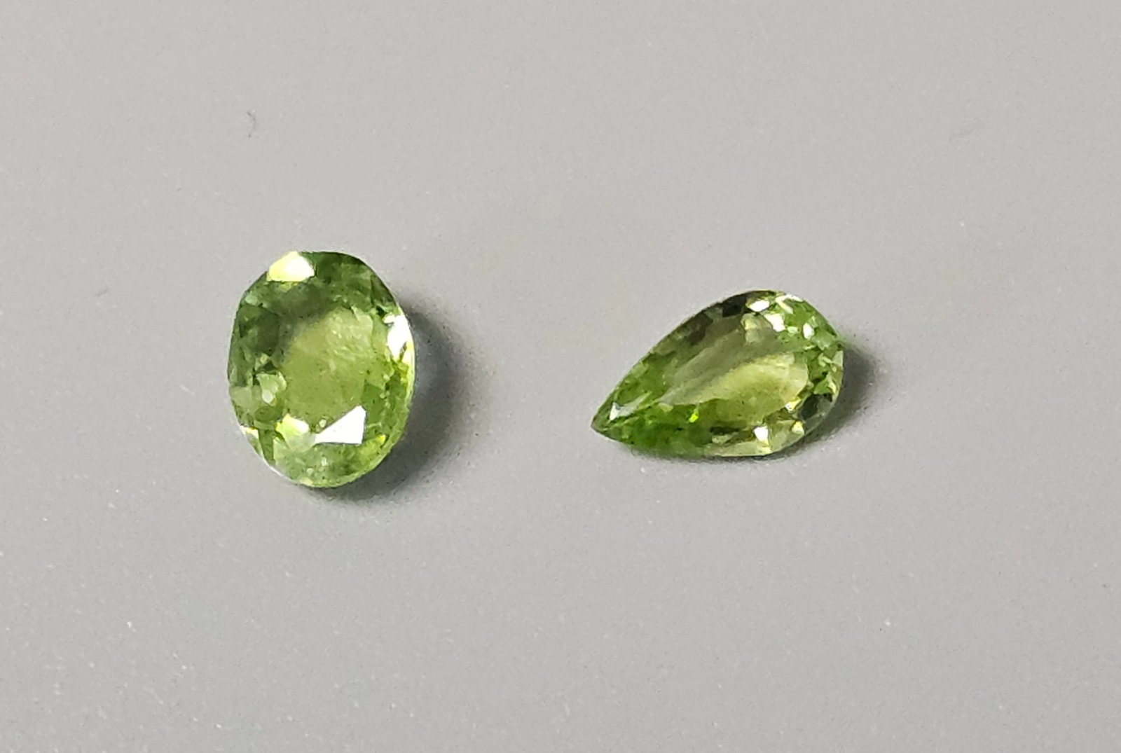Two Loose Faceted Peridot Gemstones: This lot consists of two loose, faceted peridot gemstones featuring one oval-cut and one pear-cut specimen. Oval stone measures approximately 7mm by 5mm; pear stone measures approximately 7mm by 4mm.