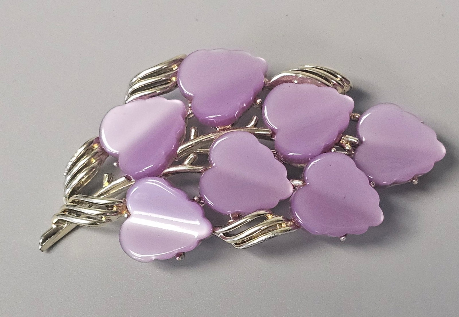 Coro Lavender Moonglow Leaf Brooch: A silver-tone costume jewelry brooch by Coro featuring a spray of seven molded lavender Lucite leaves. Length: Approximately 2.7 inches. Width: Approximately 1.25 inches at the widest point. All