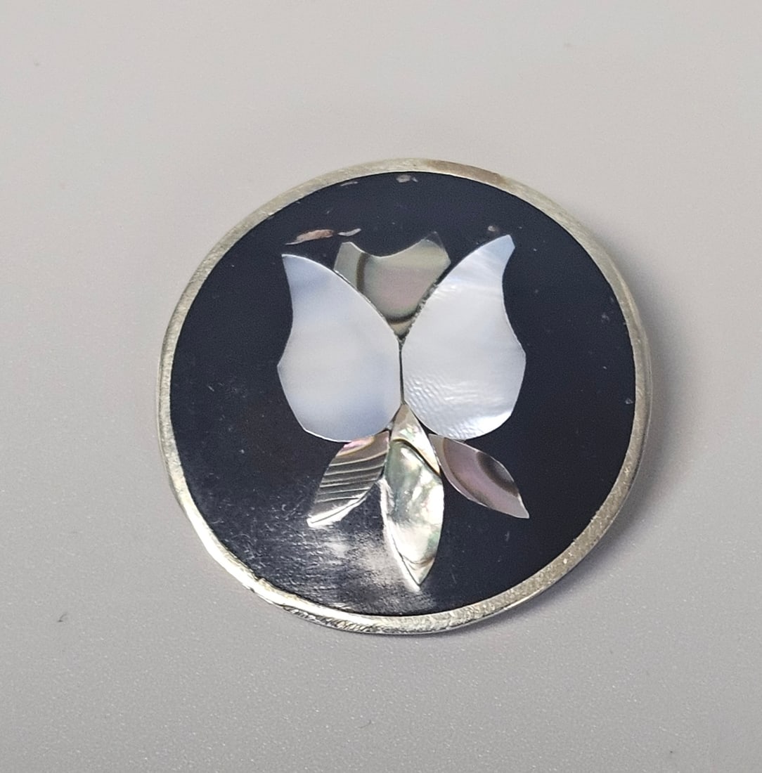 Mexican Silver and Inlay Brooch 4.9 Grams: A mid-century Mexican circular brooch and pendant combination featuring a stylized floral motif in iridescent abalone and mother-of-pearl inlay. Weighing 4.9 grams, the piece retains its Good vintage