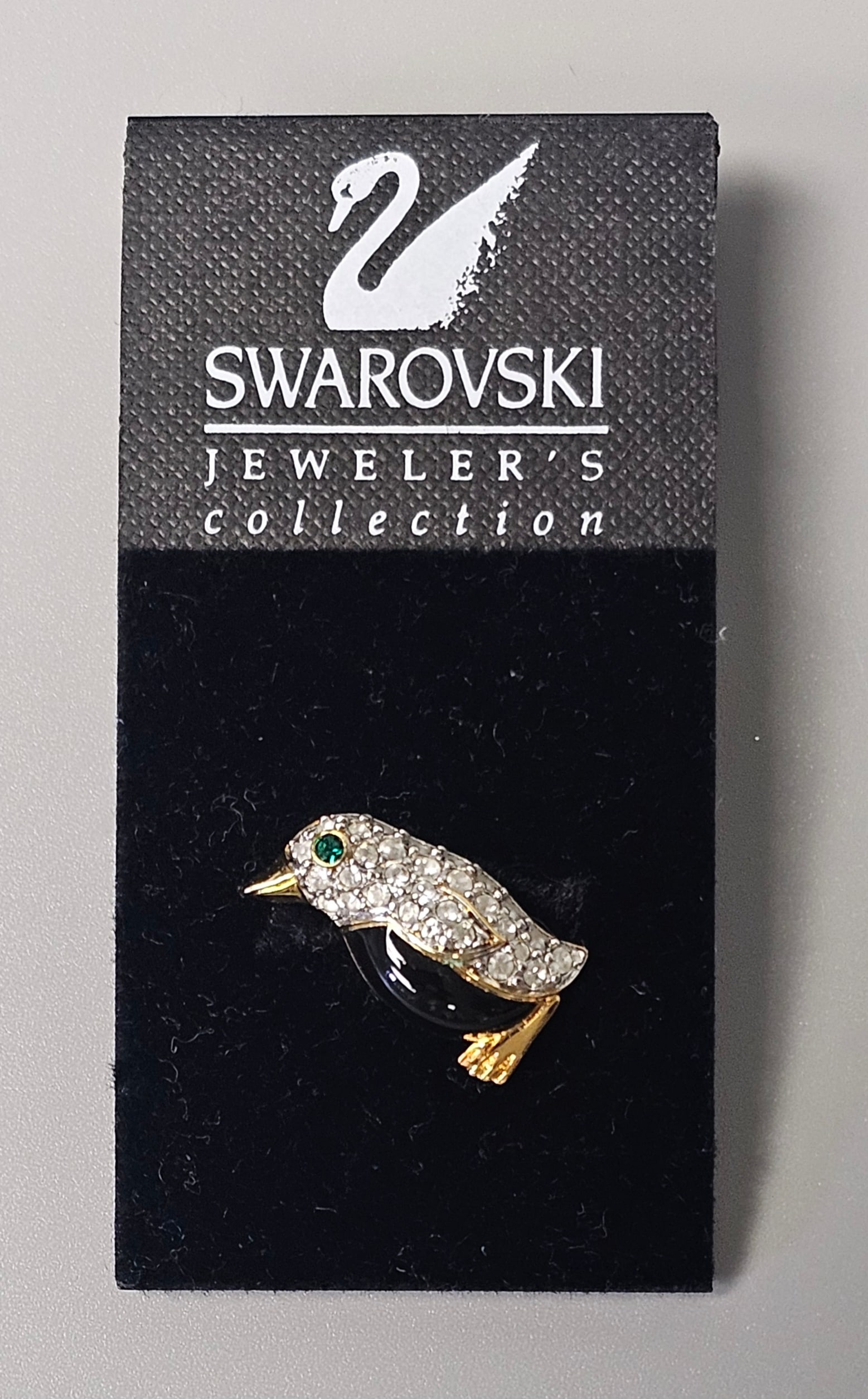 Swarovski Gold-Tone Crystal Penguin Pin: A Swarovski Jeweler's Collection figural pin featuring a stylized penguin motif. The bird's head and wings are decorated with pave-set colorless crystals, accented by a single circular faceted green