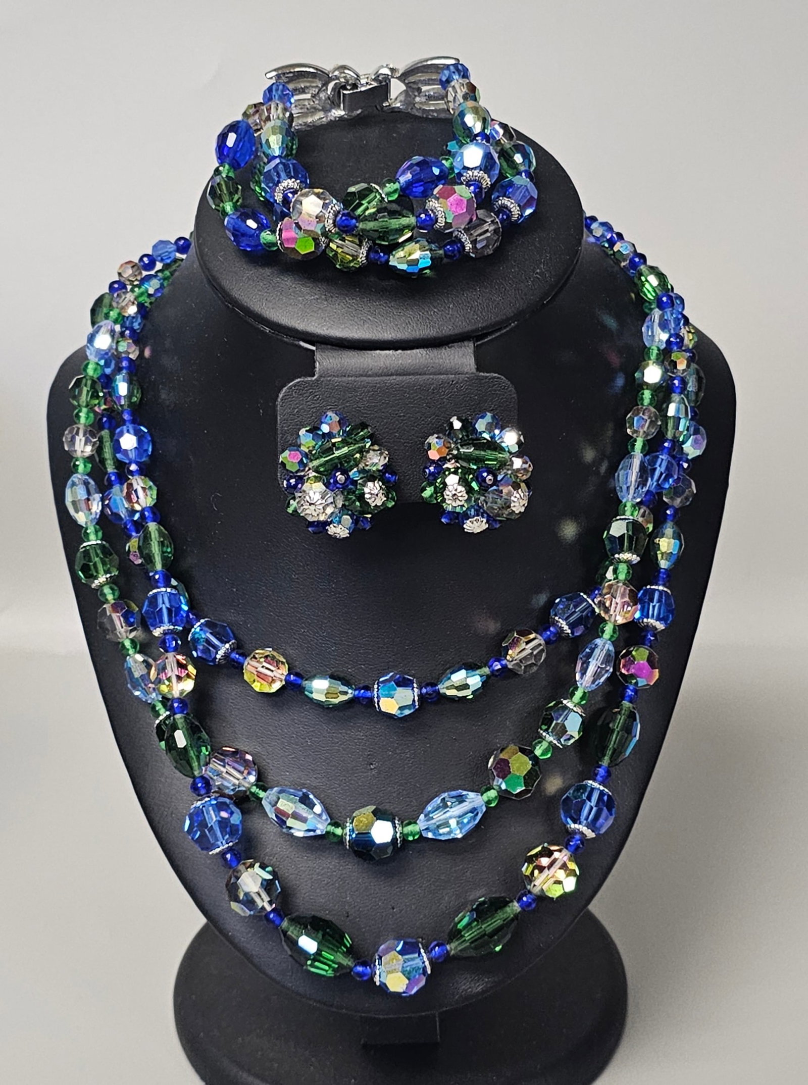 Avon Silver-Tone Faceted Glass Jewelry: An assortment of vintage costume jewelry featuring a triple-strand necklace, a matching triple-strand bracelet, and a set of coordinating cluster earrings. The pieces are crafted with faceted glass be