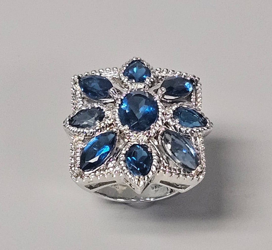 IST Sterling Blue Cluster Cocktail Ring 9.5 Grams: A sterling cocktail ring featuring a tiered cluster of faceted blue stones in a floral star motif. The arrangement consists of a central oval-cut blue stone surrounded by eight marquise-cut blue