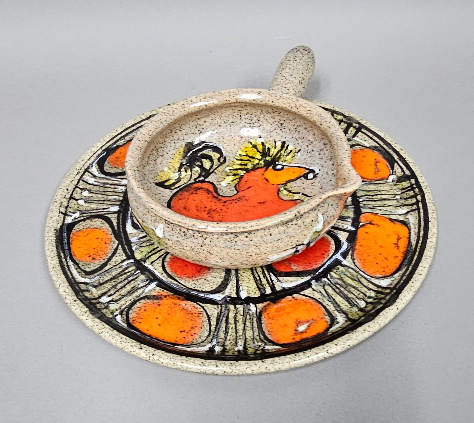 Speckled Earthenware Hand-Painted Rooster Pipkin & Plate: This two-piece hand-painted studio pottery set includes a flat charger plate and a matching pipkin-style bowl. Crafted from heavy speckled earthenware with an oatmeal-colored glaze, the set features