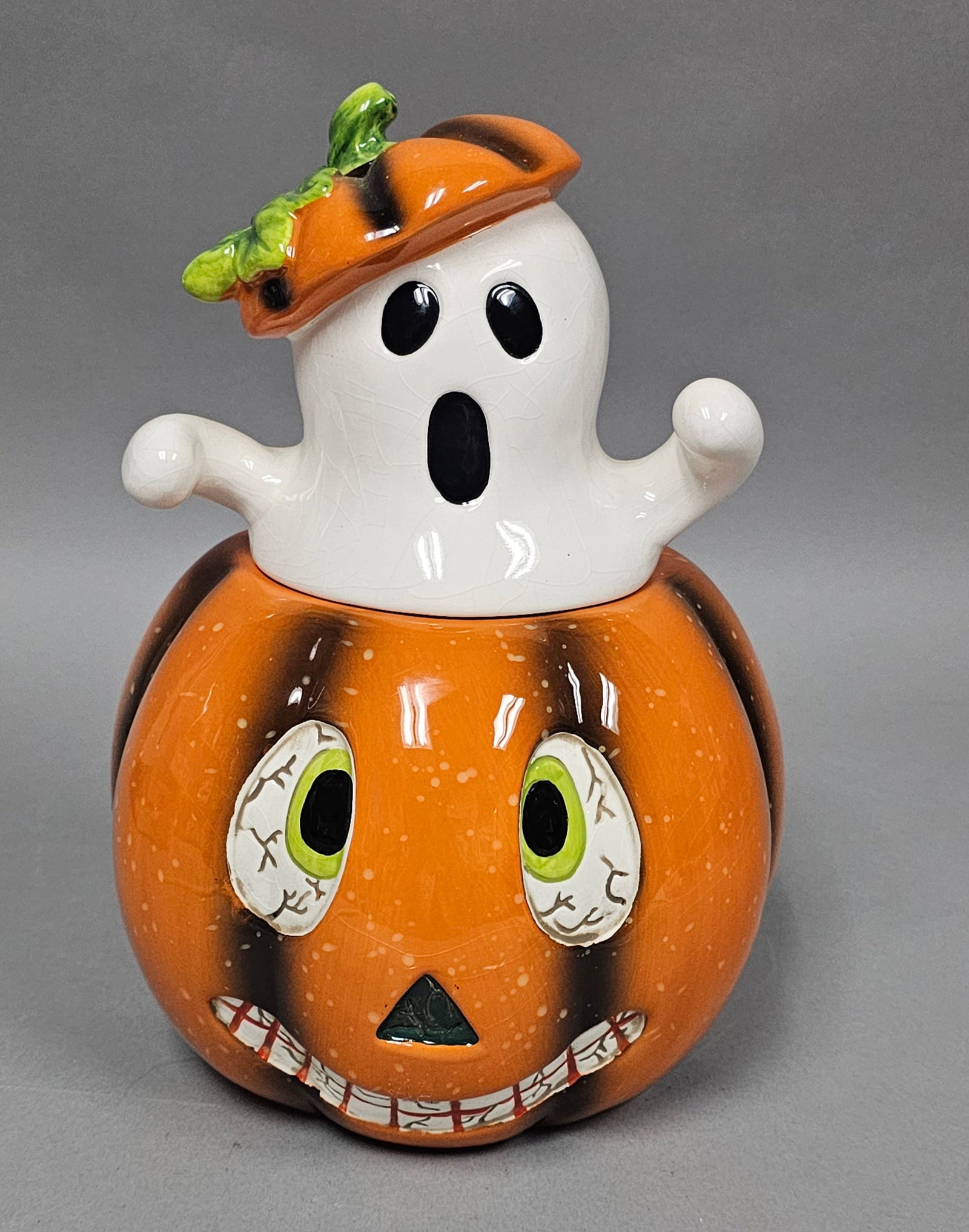 Wholesale Merchandisers Ceramic Halloween Cookie Jar: An earthenware two-piece Halloween cookie jar featuring a jack-o'-lantern base and a removable ghost lid. Height: 10.5 inches The cookie jar is in good vintage condition with no visible chips, cracks,