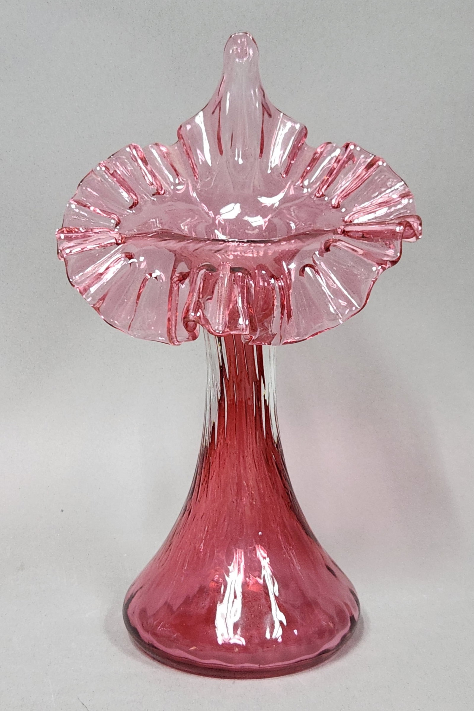 Fenton Cranberry Jack-in-the-Pulpit Vase: Fenton cranberry glass Jack-in-the-pulpit vase featuring a tall neck and a wide, hand-ruffled rim. The hand-blown body is decorated with vertical optic ribbing and rests on a weighted base with a